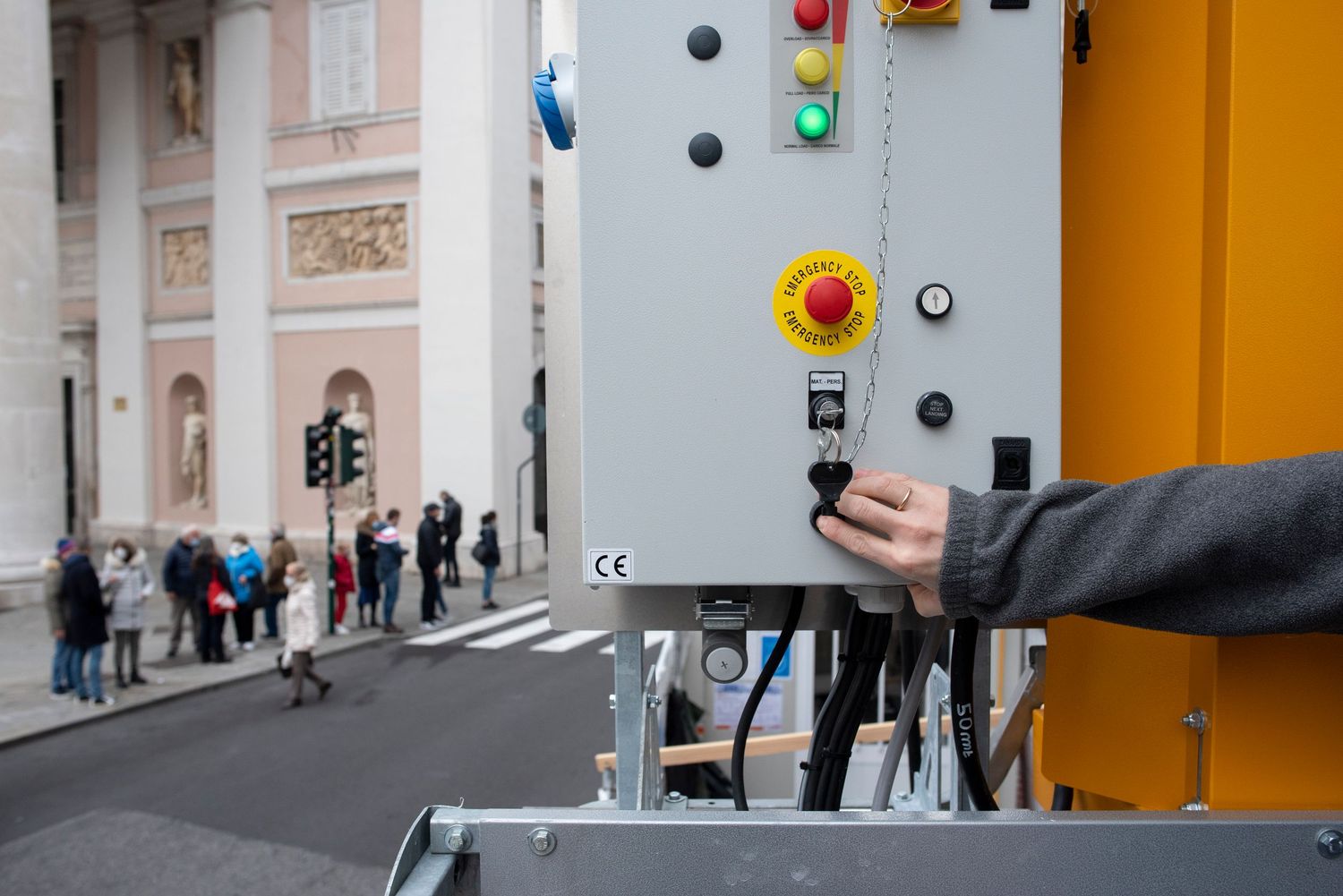 A hand operates a yellow industrial control panel with emergency stop button on a city street.