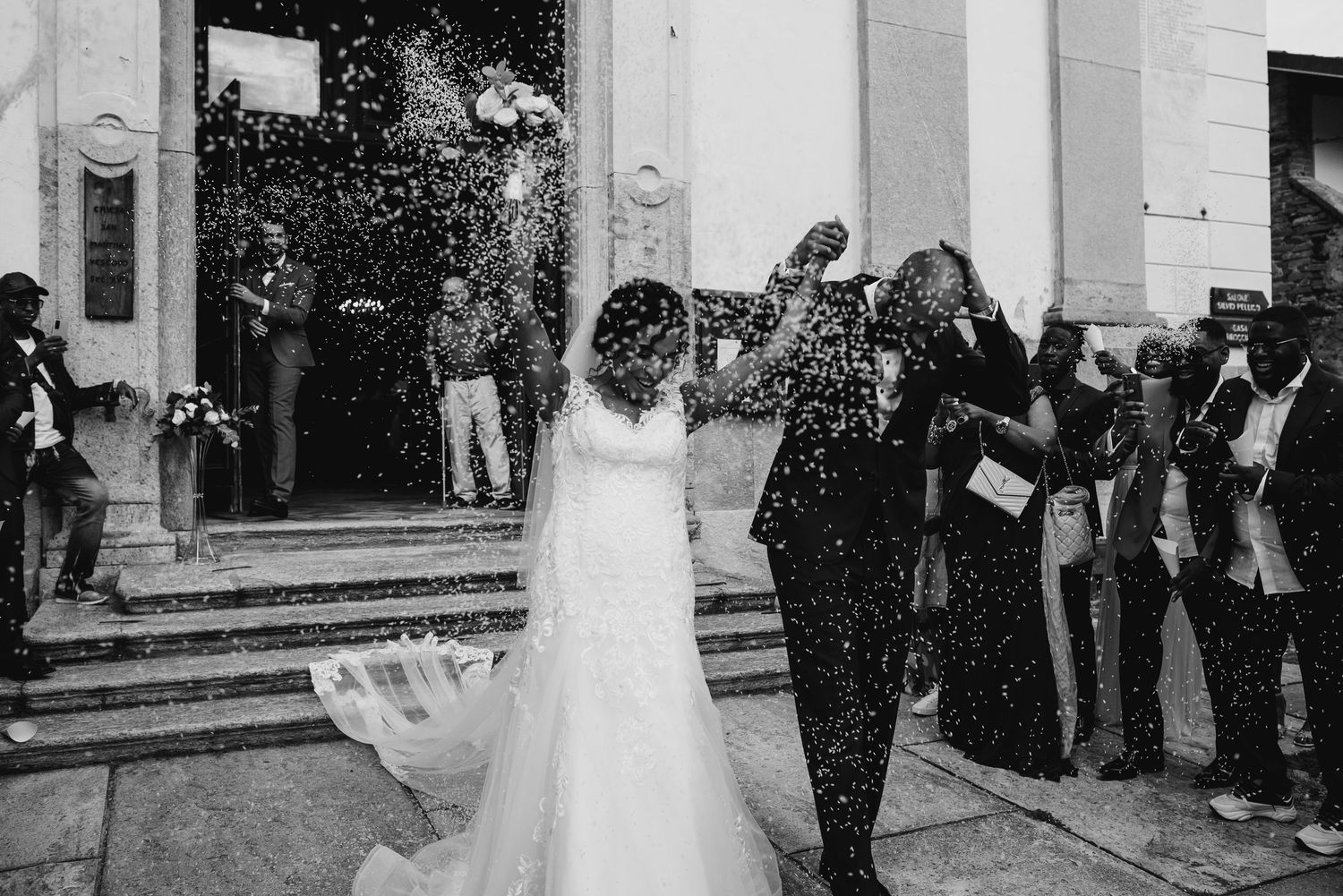 Black and white photo of a joyful couple exiting a church amid a shower of confetti on their wedding day.