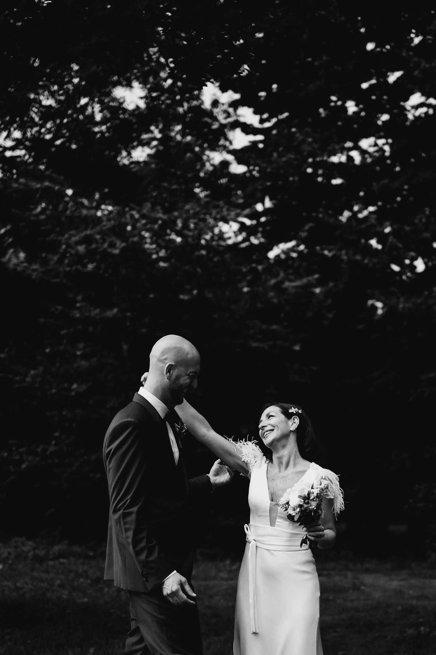 Black and white outdoor wedding scene with dramatic lighting through trees.