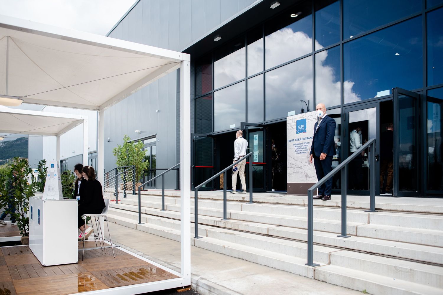 Modern conference center entrance with glass facade, steps, railings, and a large portrait banner outside.