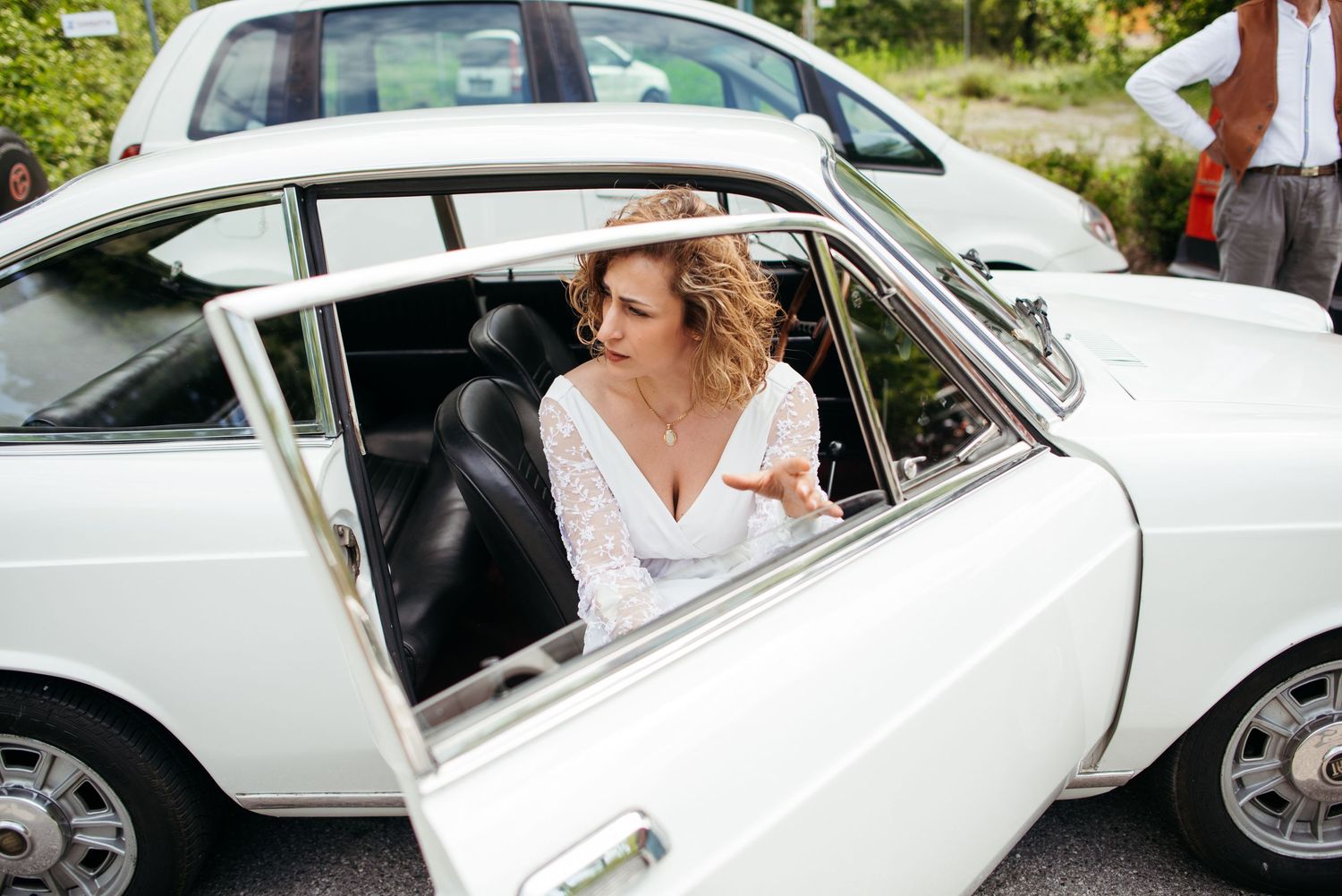 A classic white vintage car with someone sitting in the passenger seat looking out the window.