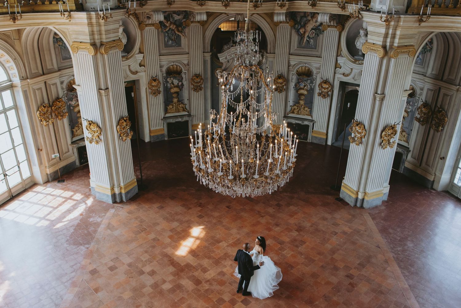 Crystal chandeliers and ornate decor adorn the grand ballroom of a luxurious historic palace.