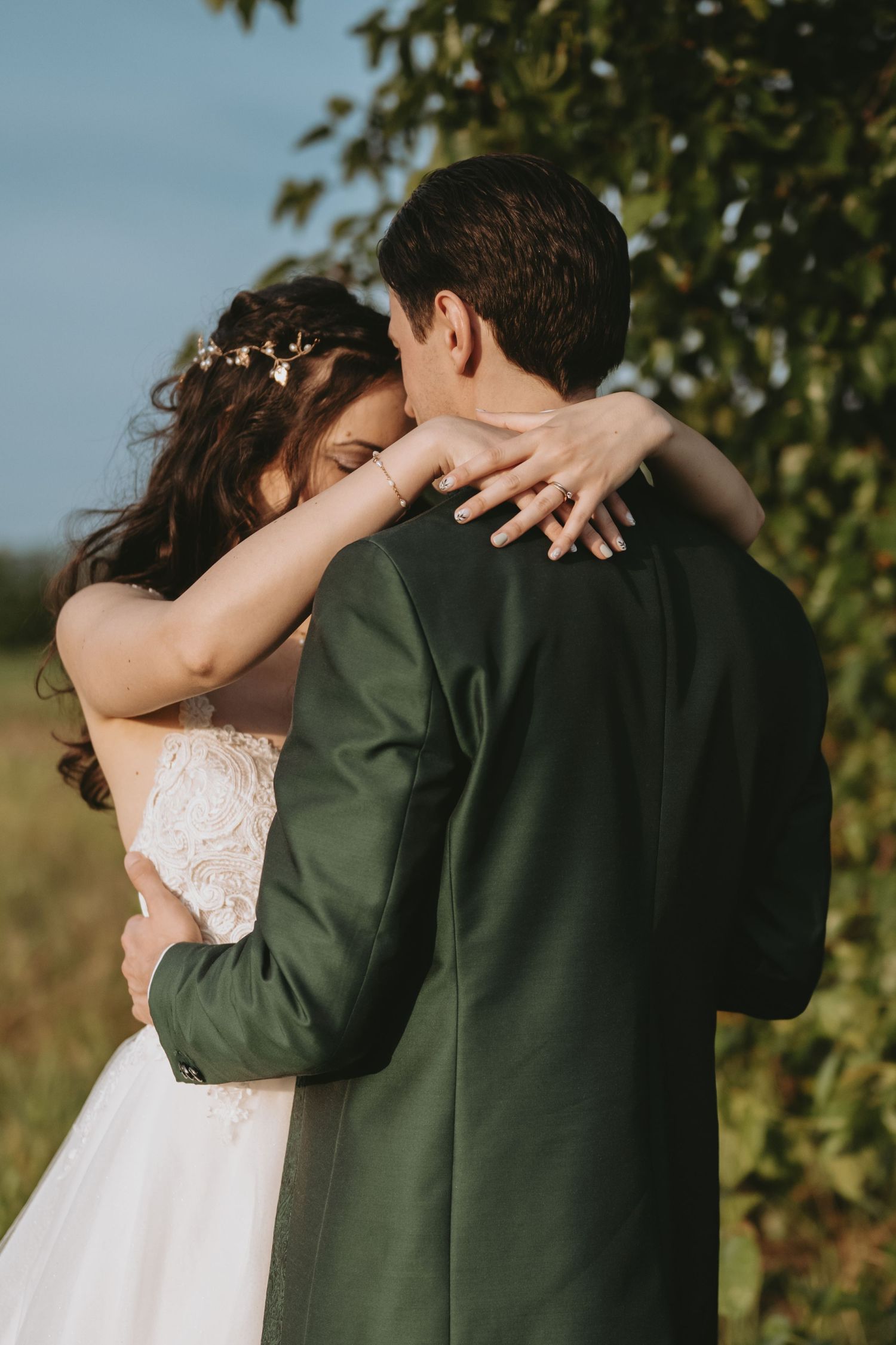 A couple embracing in a field, with the woman wearing a white dress and the man wearing a dark jacket.