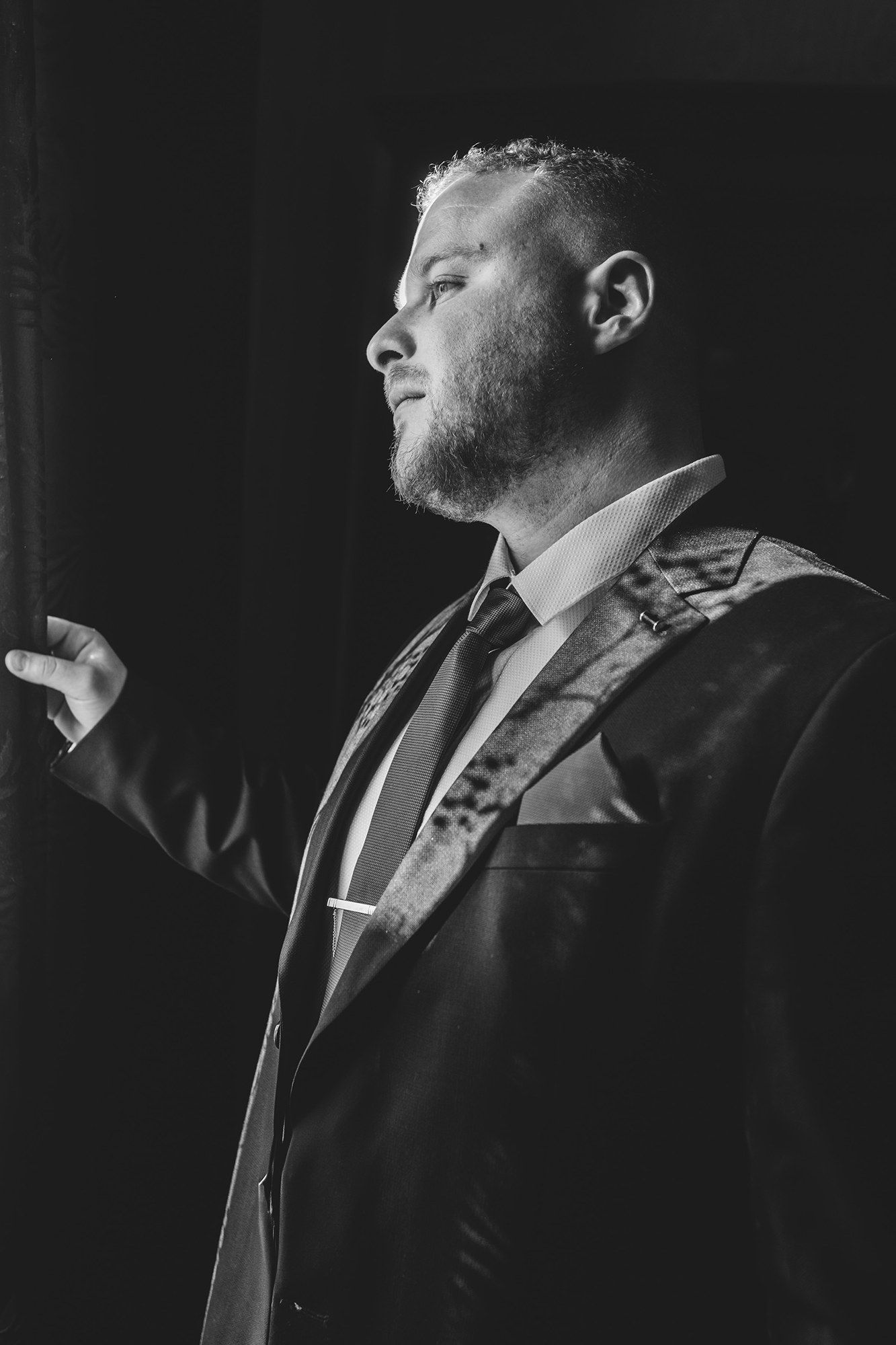 Dramatic black and white profile portrait of a man in formal attire.