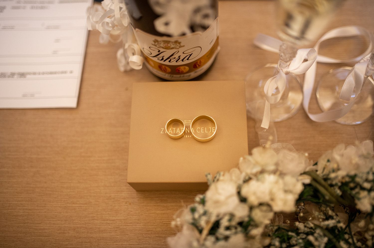 Wedding rings and decorative details on a wooden table with floral arrangements.