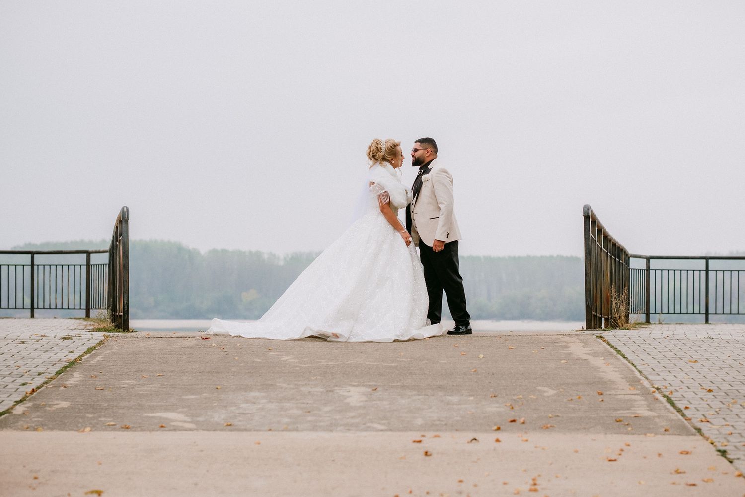Wedding couple poses on stone walkway with scenic waterfront backdrop.