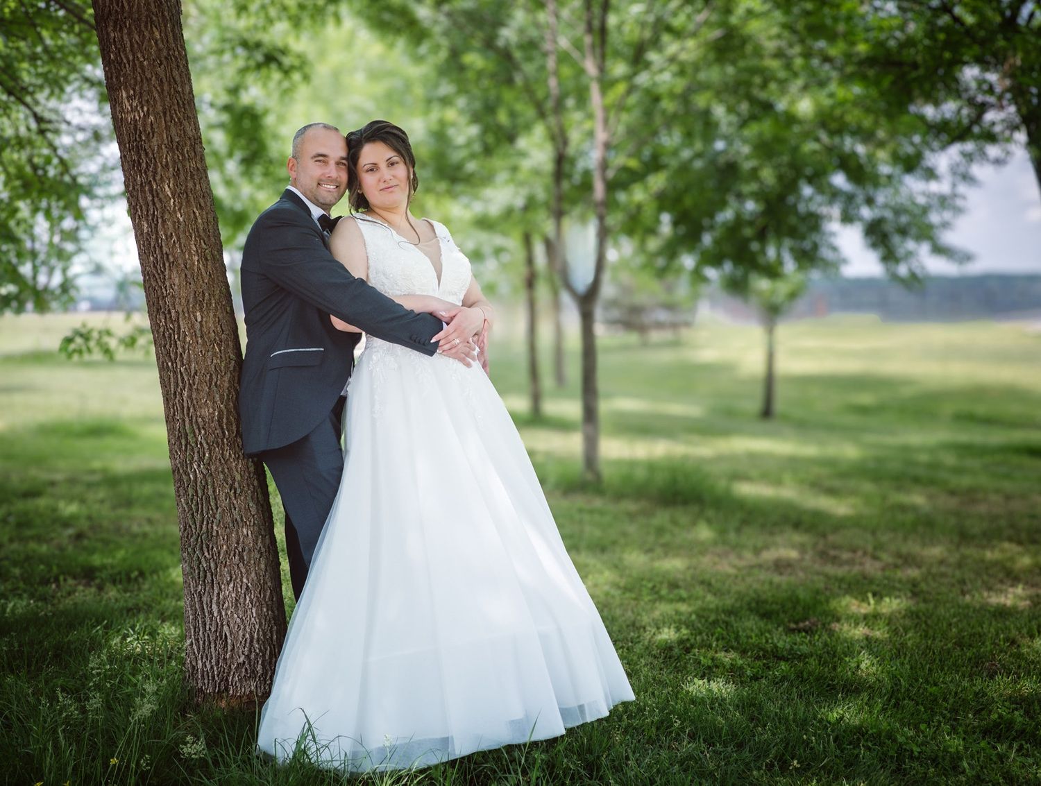 Romantic wedding portrait under trees in a lush green outdoor setting.