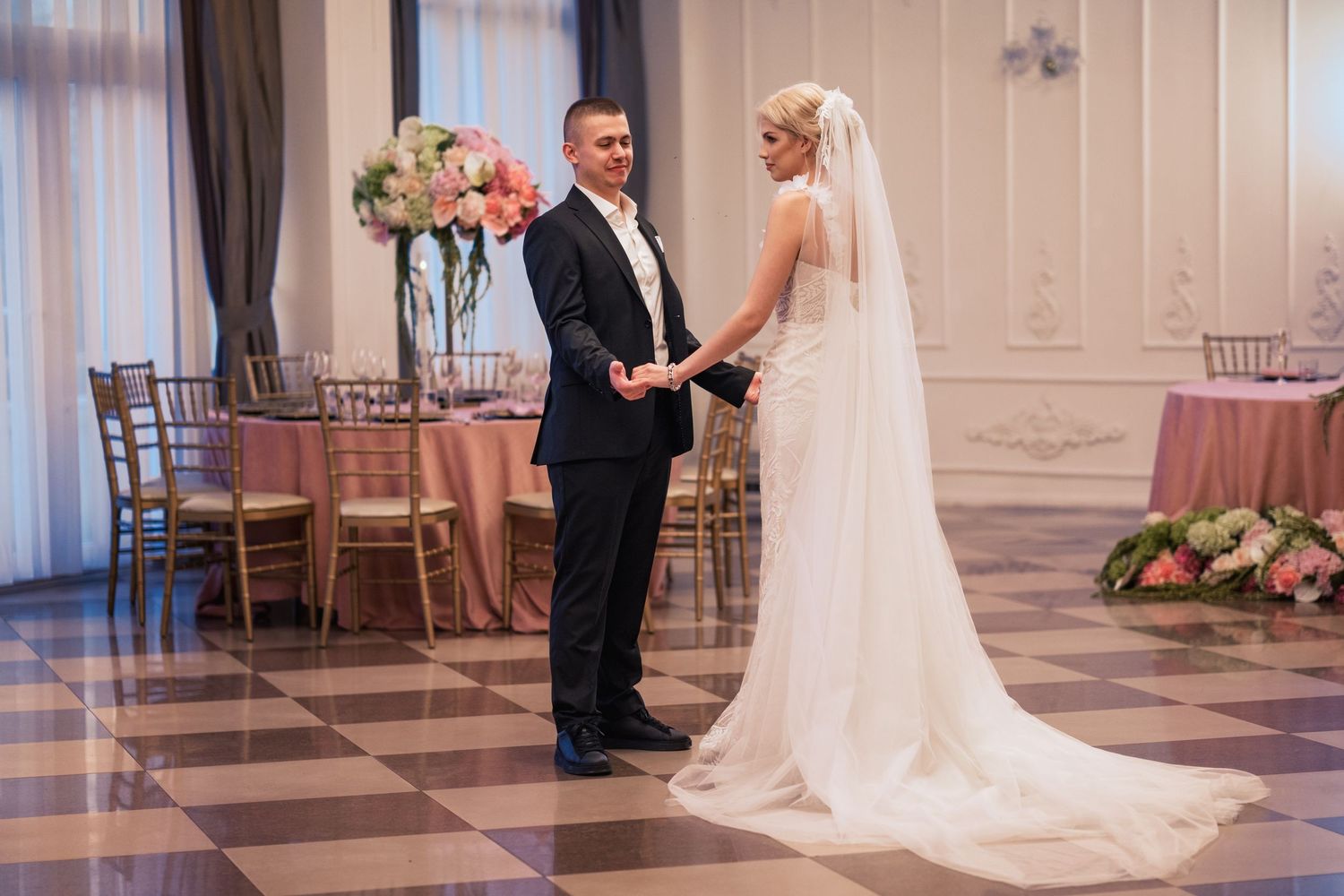 Elegant wedding ceremony in a grand room with checkered floors and floral arrangements.
