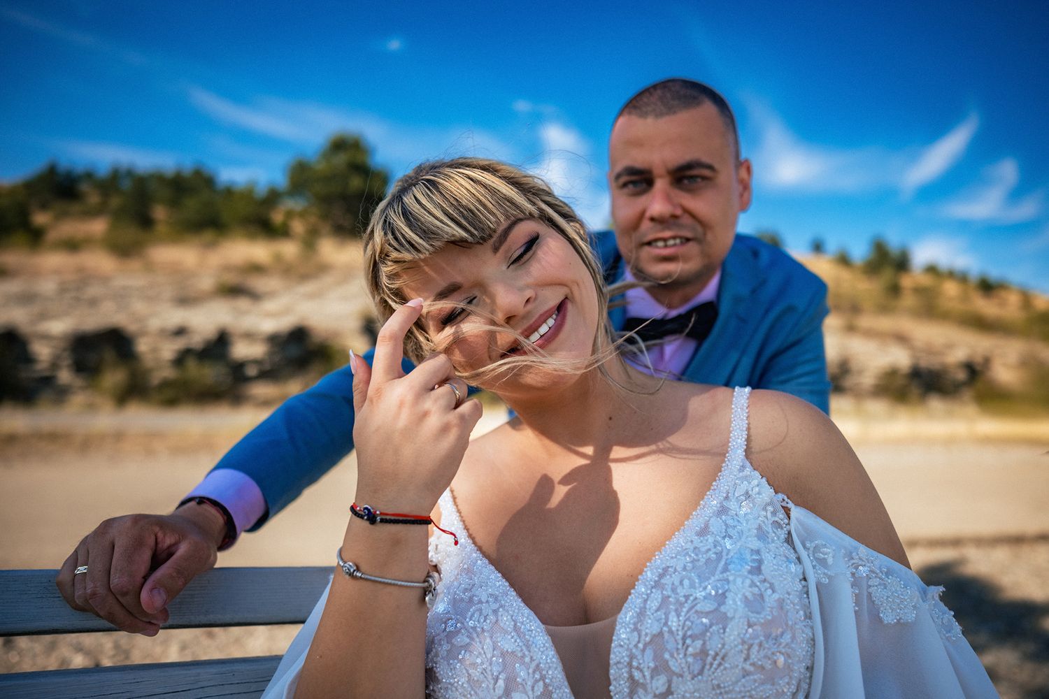 A couple embraces during a sunny outdoor wedding celebration with mountains in the background.