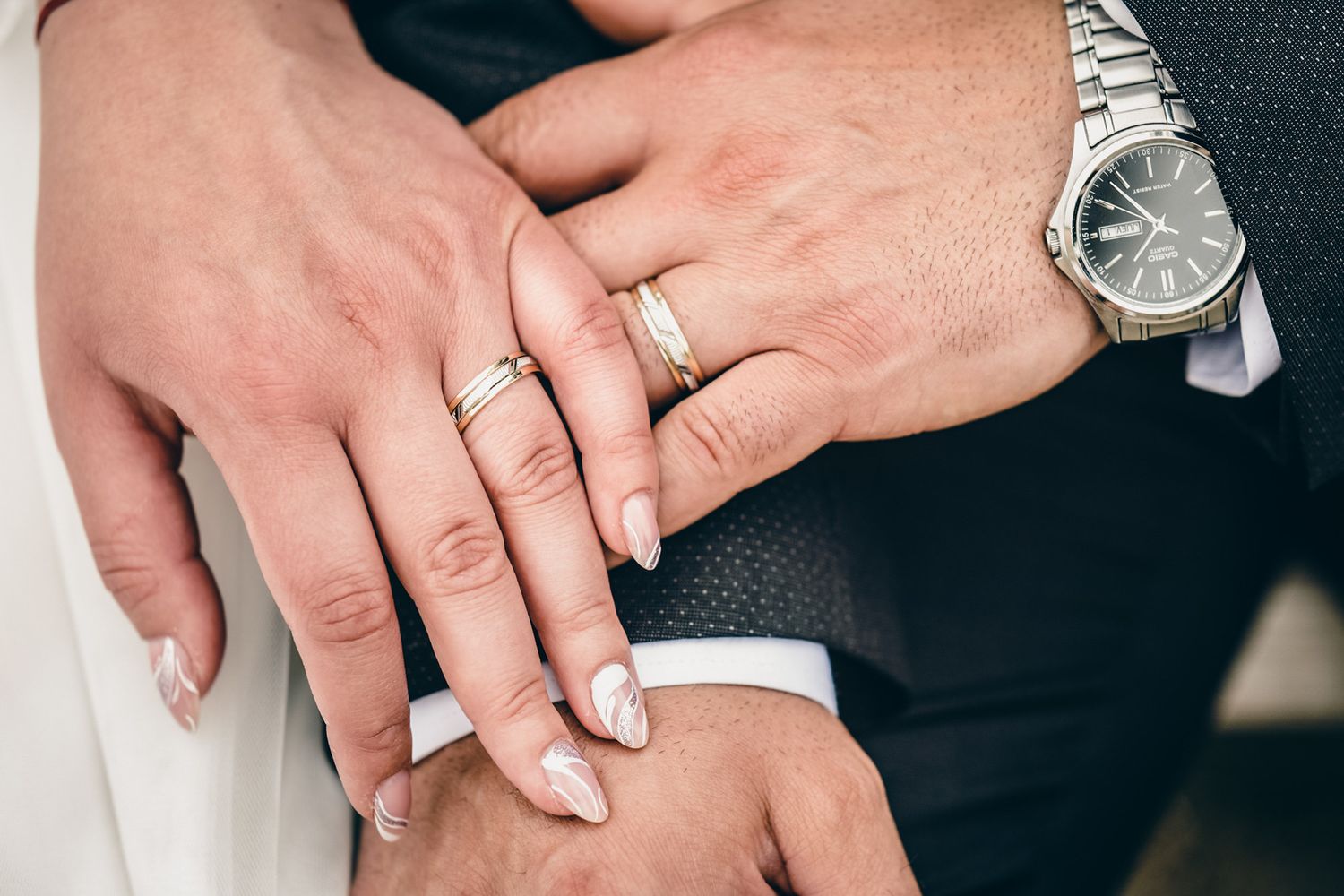 Close-up of wedding rings and a watch as newlyweds hold hands.