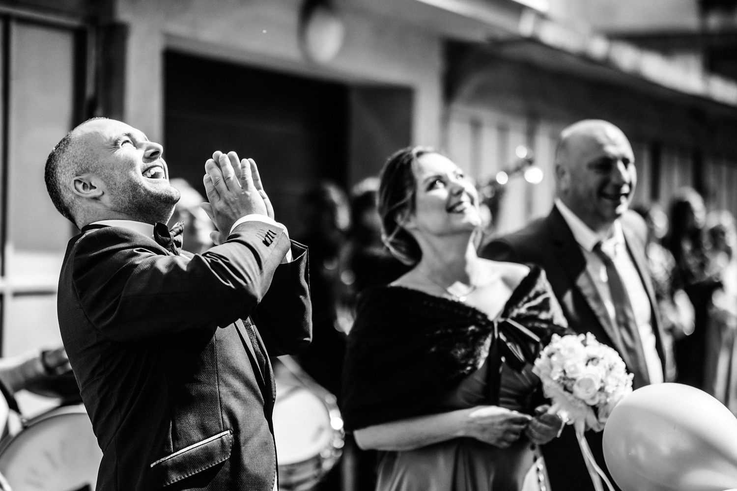 Black and white candid shot of wedding guests laughing joyfully outdoors.