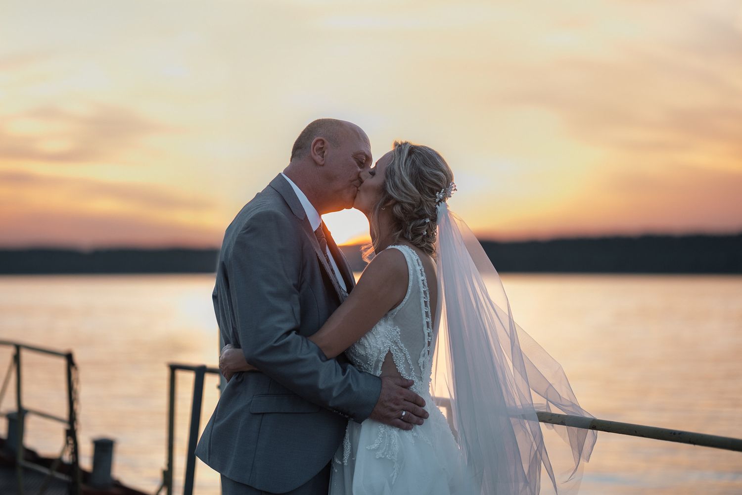 Romantic sunset wedding ceremony by the water with warm orange sky.