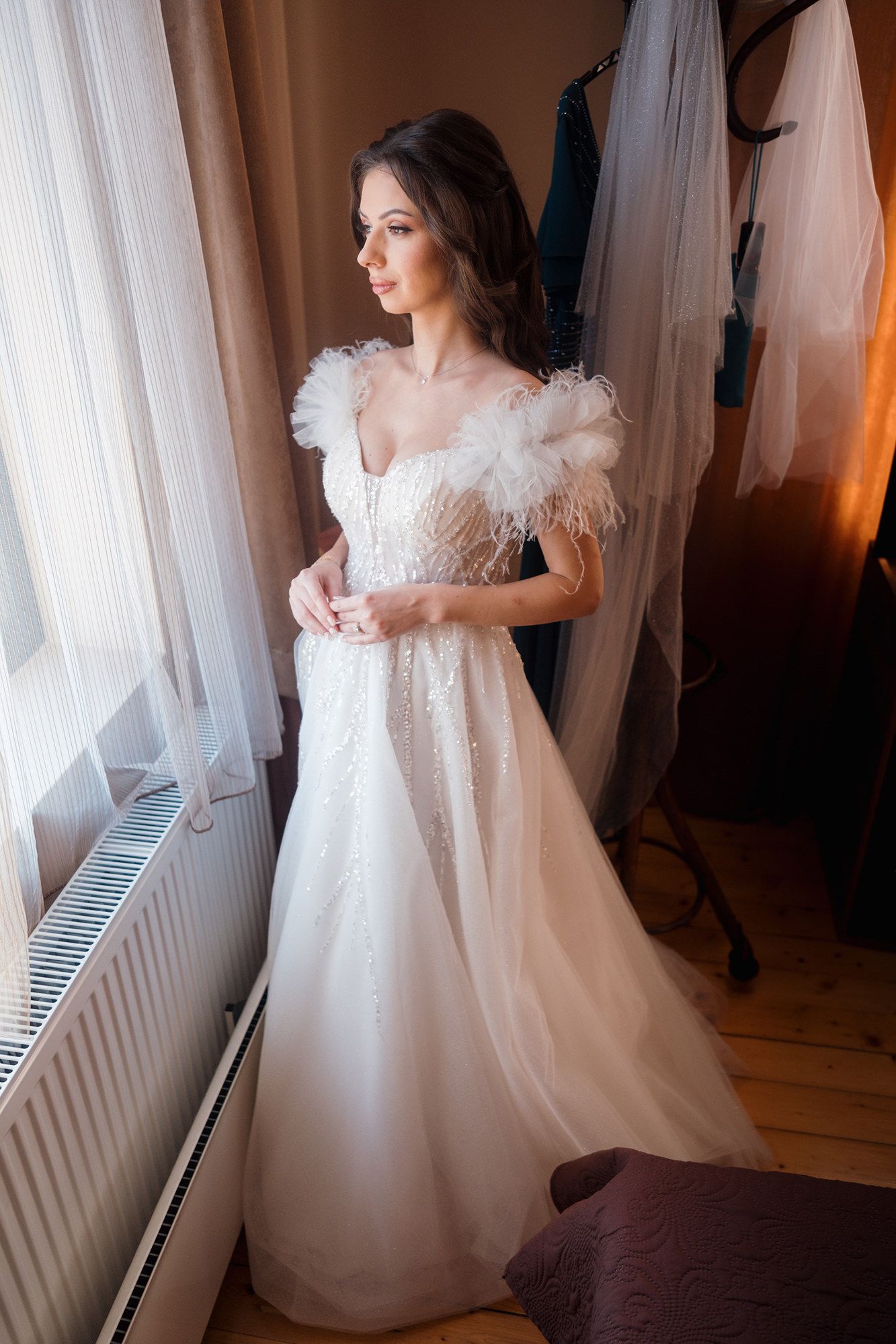 Bride in flowing white wedding dress with feather details prepares for her special day.