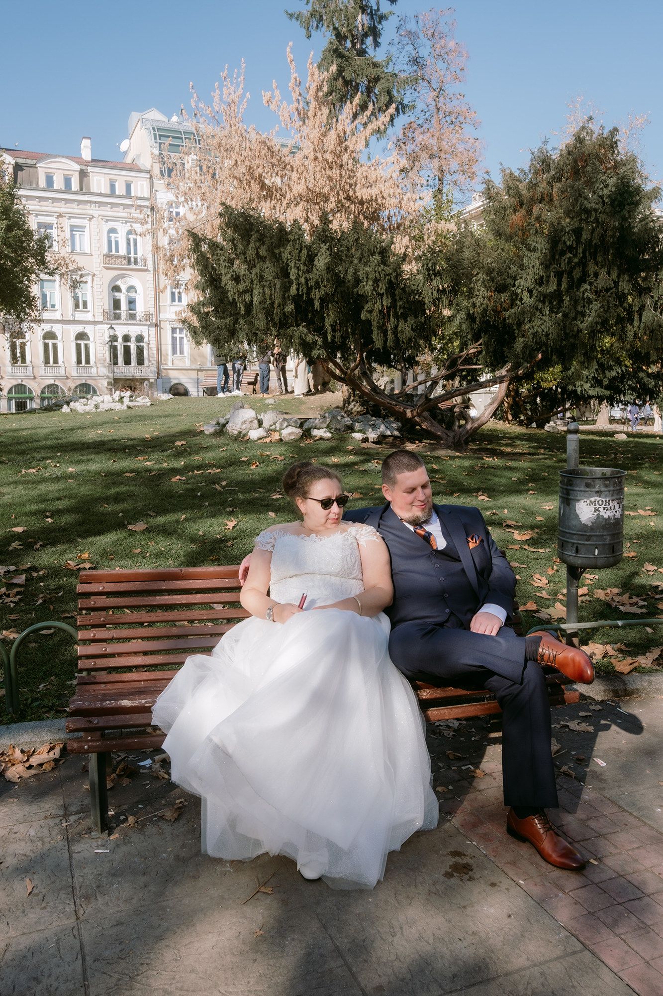 Couple relaxing on park bench with historic building in background.
