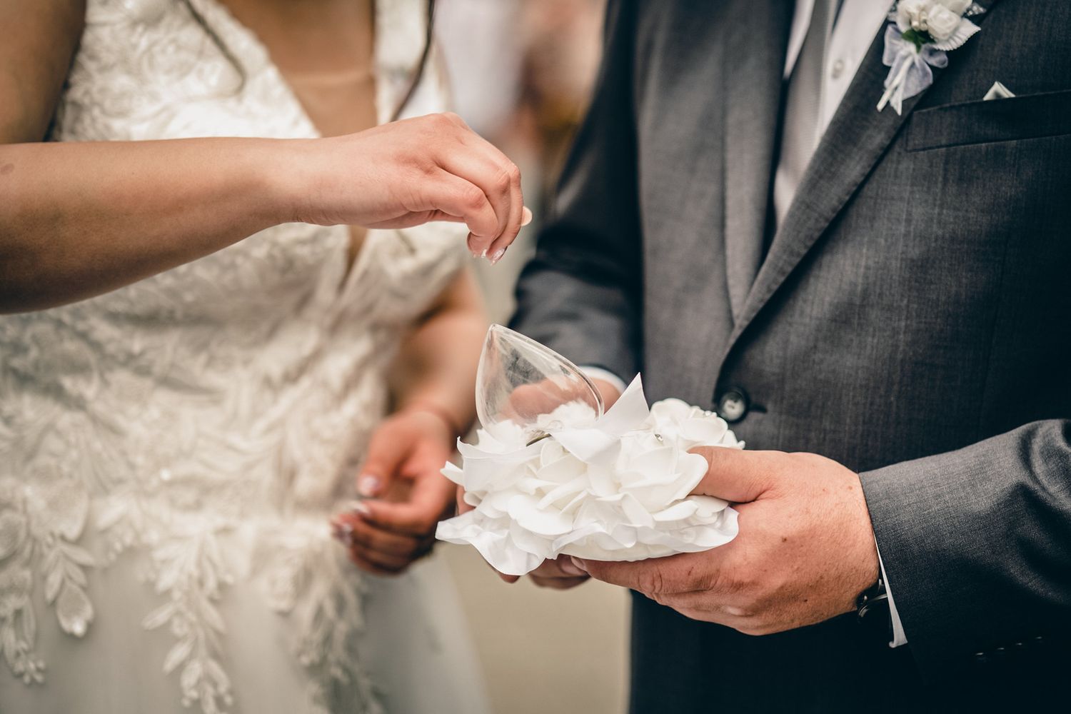 Close-up of hands exchanging decorative white paper during wedding ceremony.
