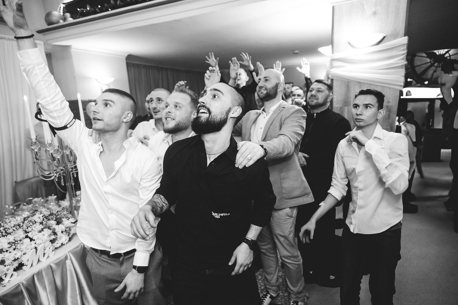 Black and white candid shot of wedding guests celebrating with enthusiastic expressions.
