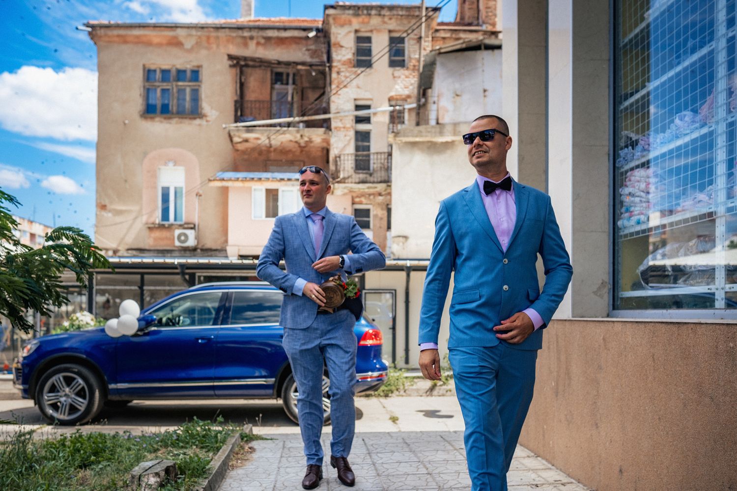 Men in blue suits walking outside modern urban building.
