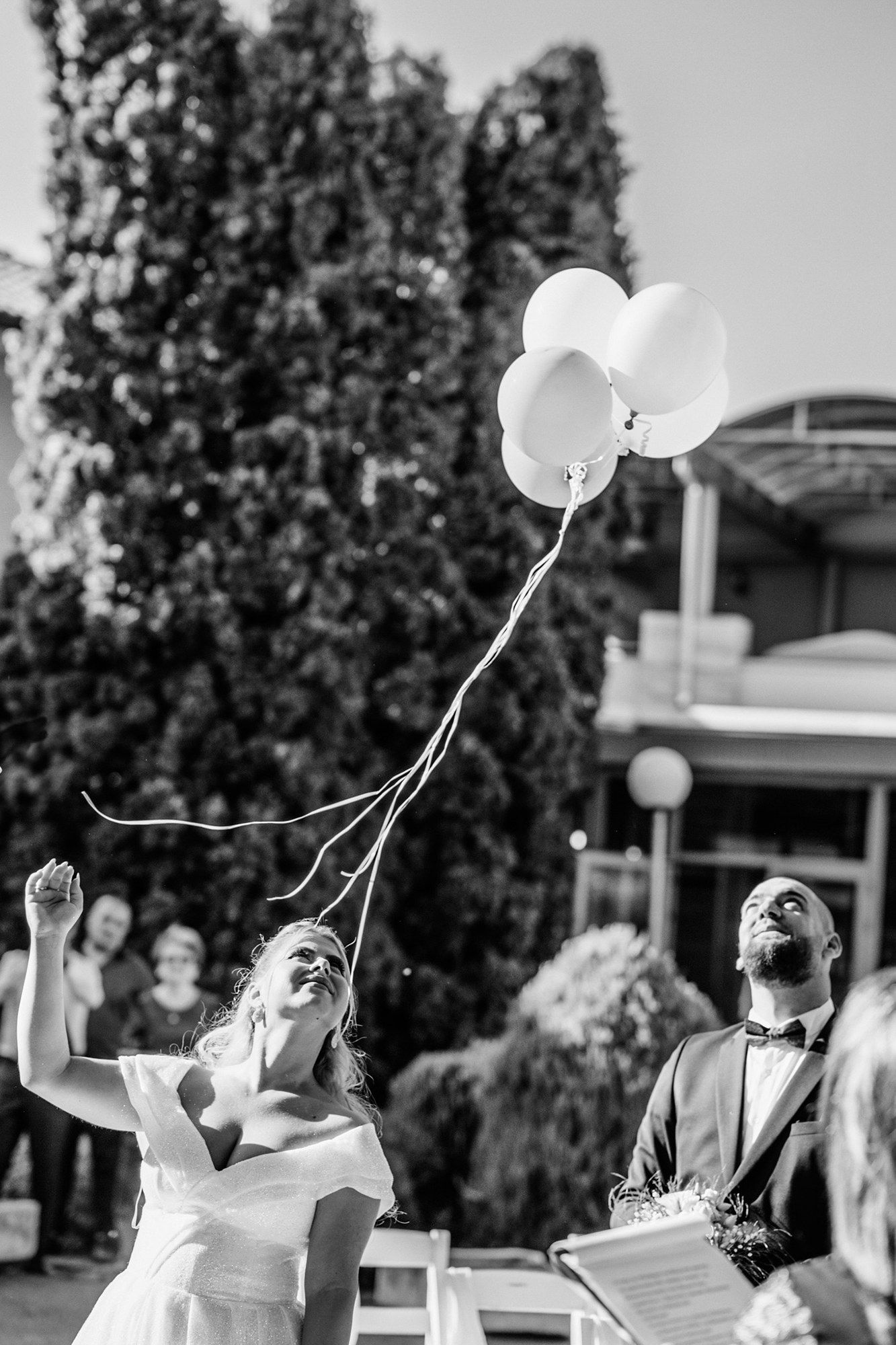 Black and white photo of newlyweds releasing white balloons during a celebration.