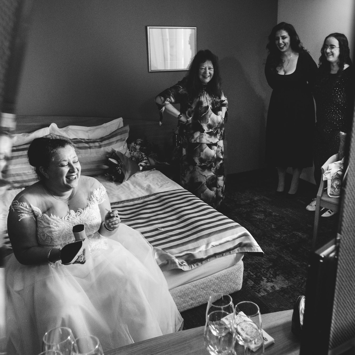 Wedding party getting ready in a room with natural light streaming through windows.
