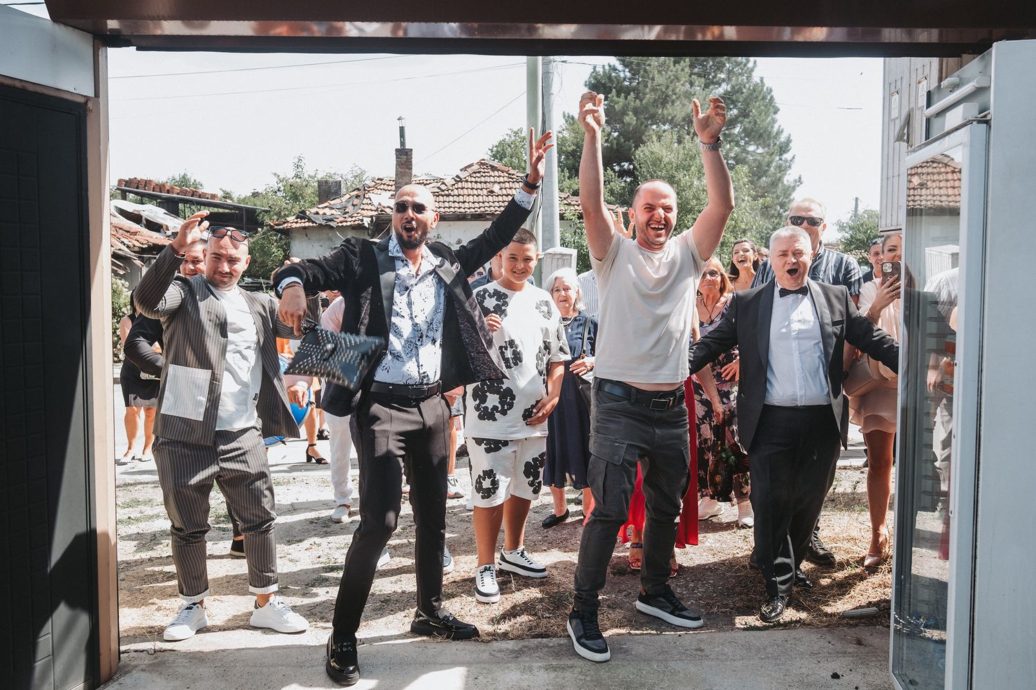 Wedding party members cheer and celebrate in a group photo outside.
