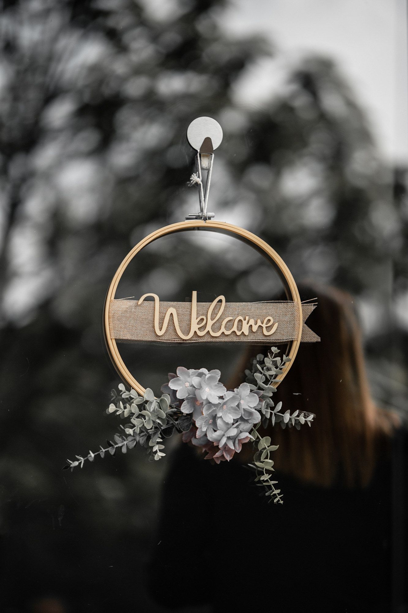 Decorative wooden welcome sign with floral accents hanging against blurred background.