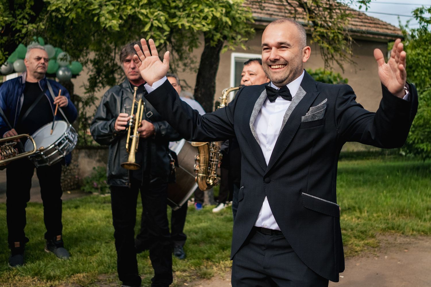 Groomsmen in black tuxedos celebrating outdoors with joyful gestures.