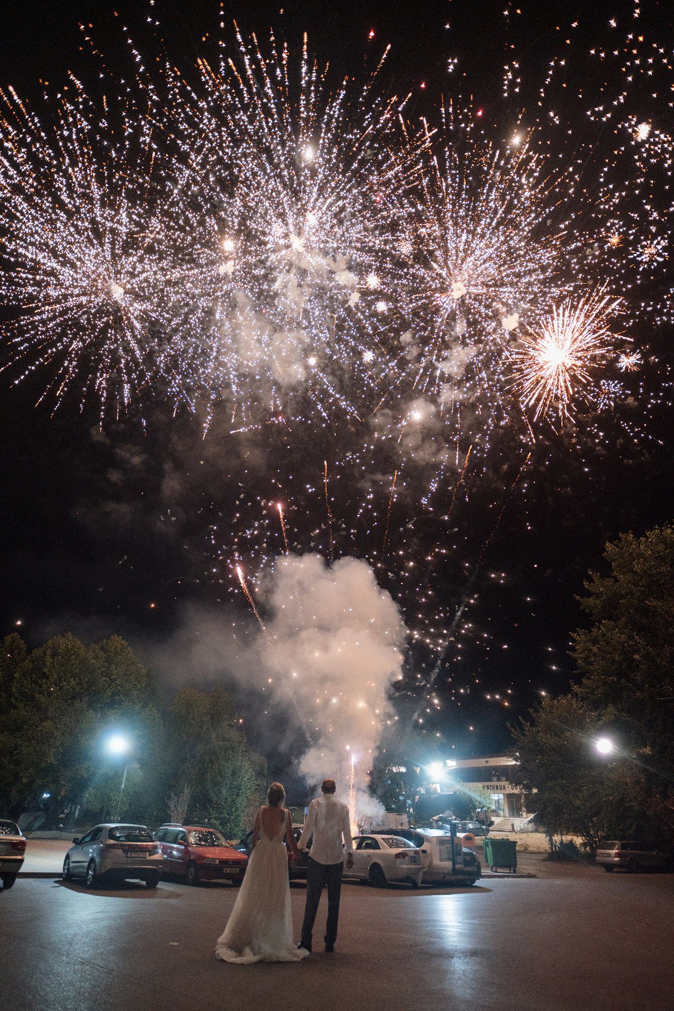 Spectacular fireworks display illuminating the night sky over a parking lot during a wedding celebration.