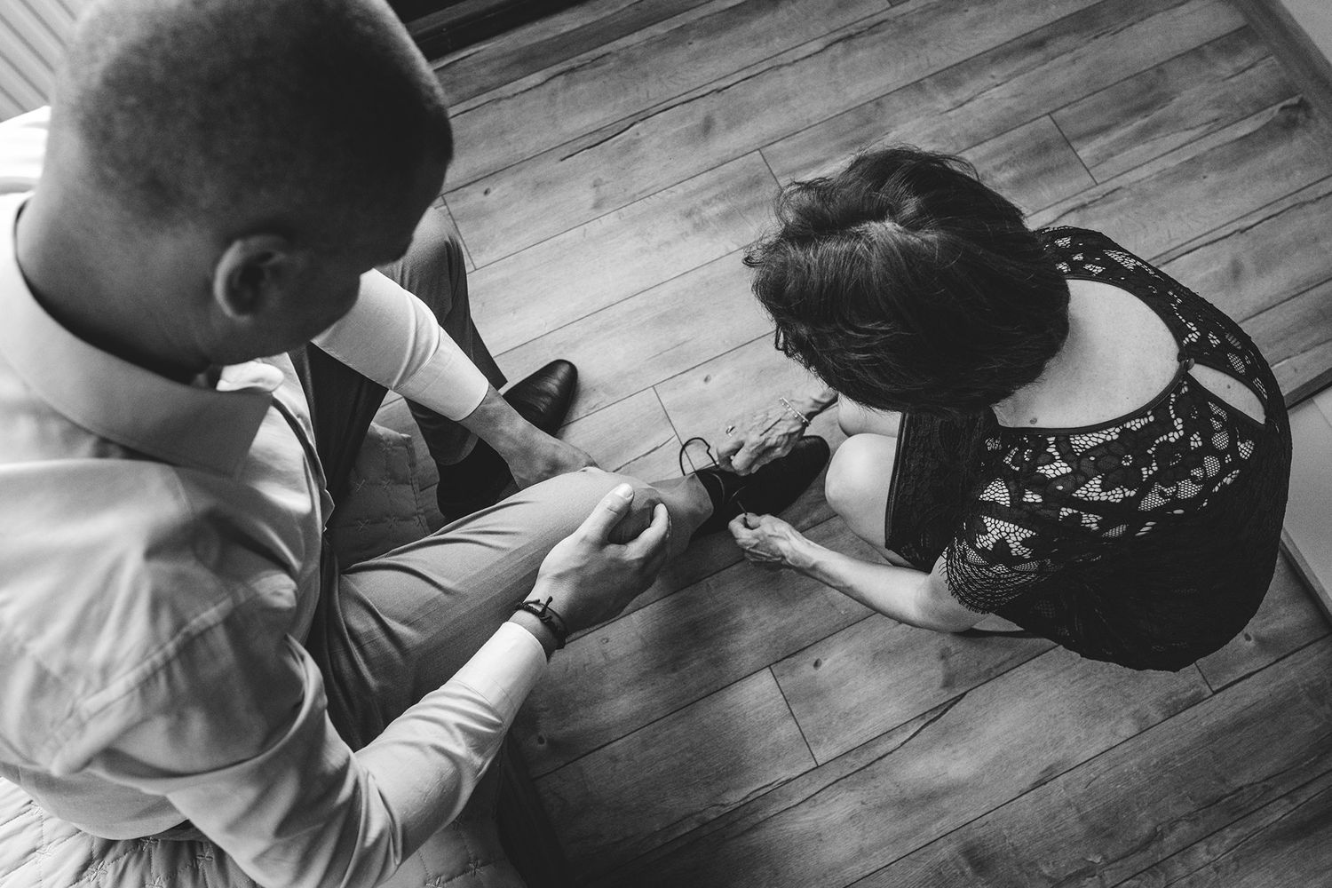 Black and white overhead view of formal shoes on wooden floor.