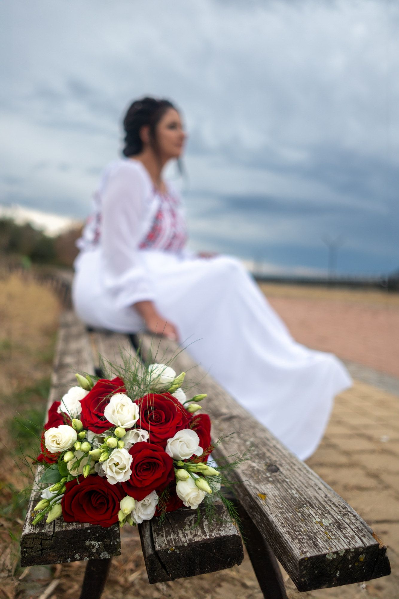 Red and white rose wedding bouquet on wooden bench with blurred background.