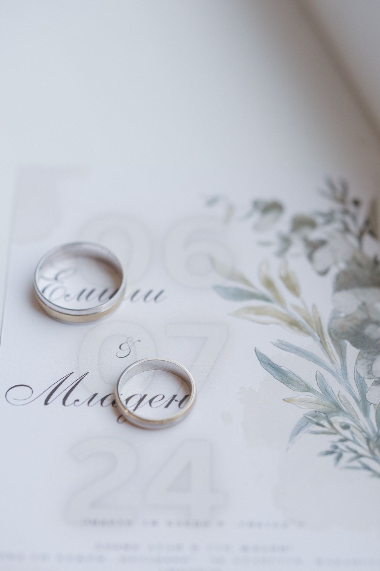 Wedding rings photographed on elegant white invitation with floral design.