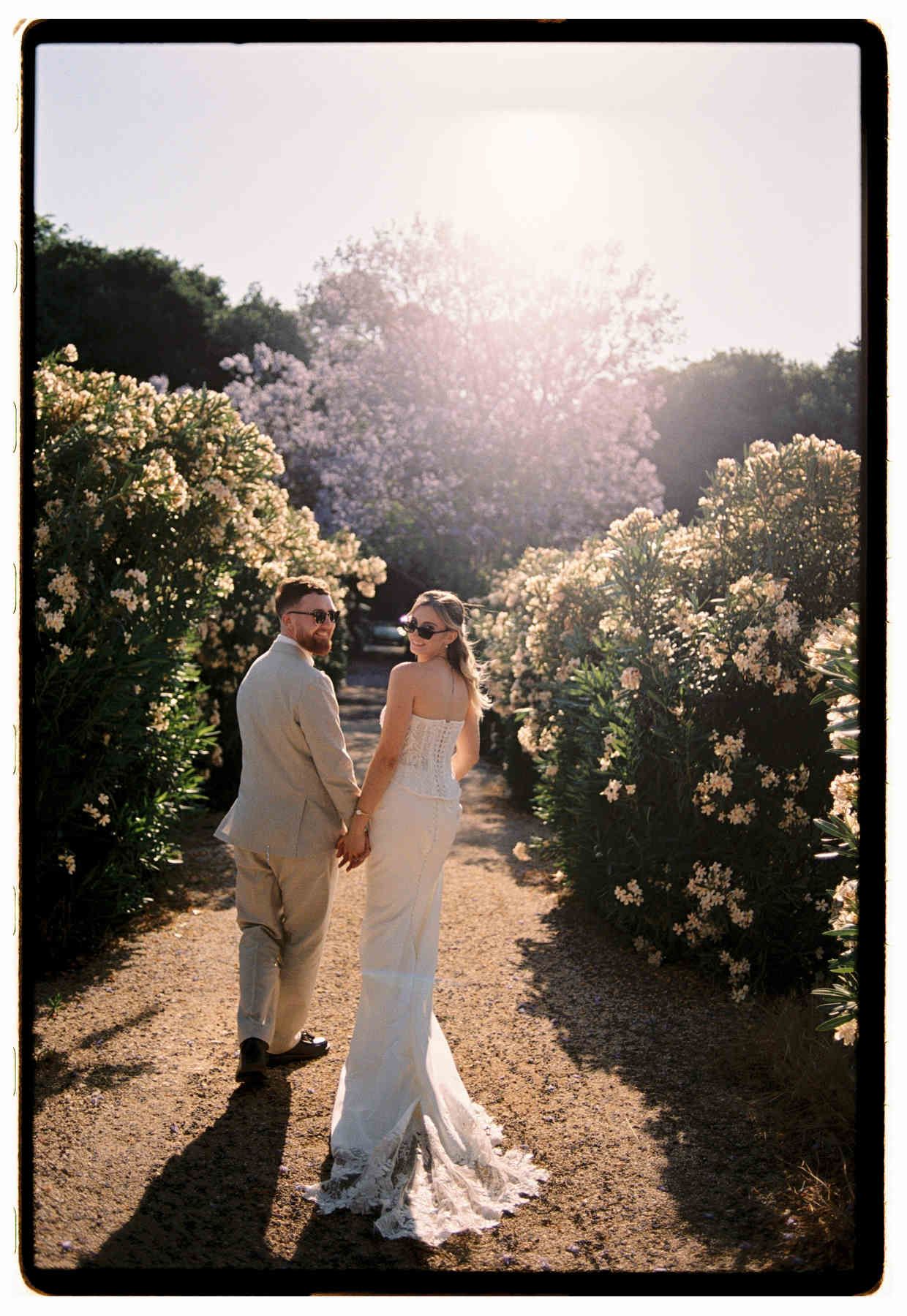 Bride and groom strolling through the lush, blooming Mediterranean gardens of Villa Delia estate.