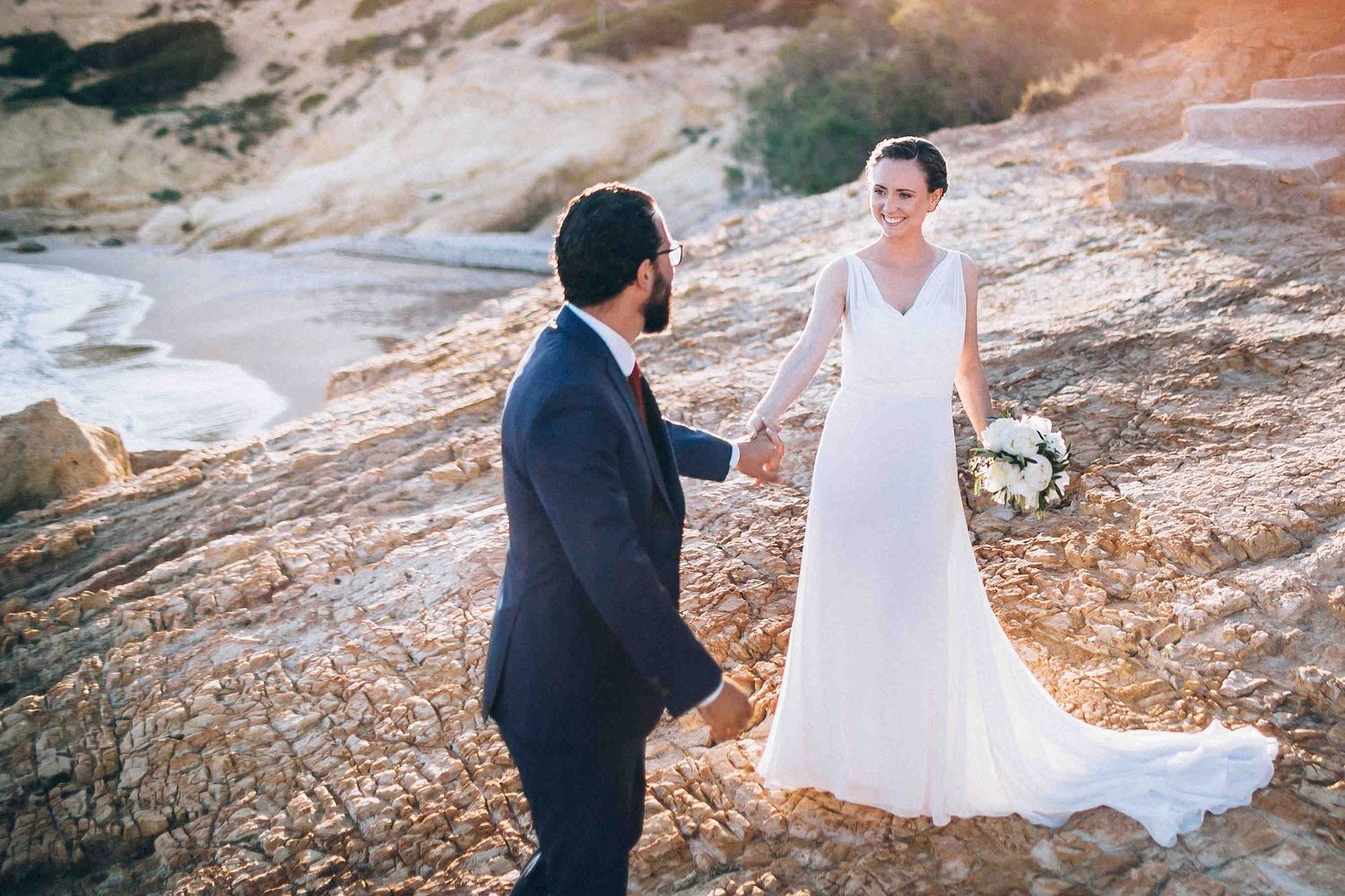 Editorial bridal portrait with a long dress train flowing on the windy beach in Greece