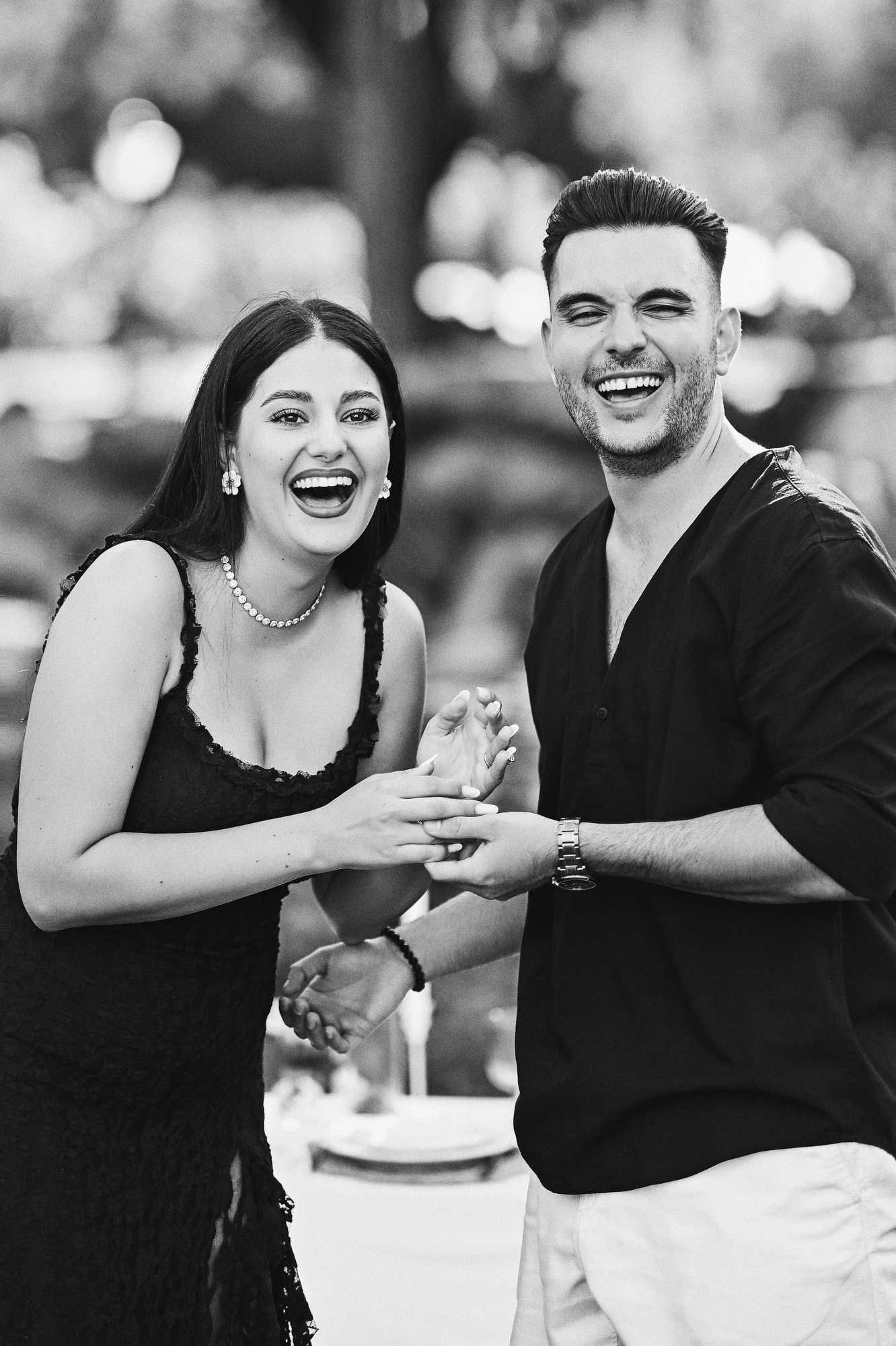 Black and white shot of a newly engaged couple laughing out loud holding hands during their Valencia park photoshoot.