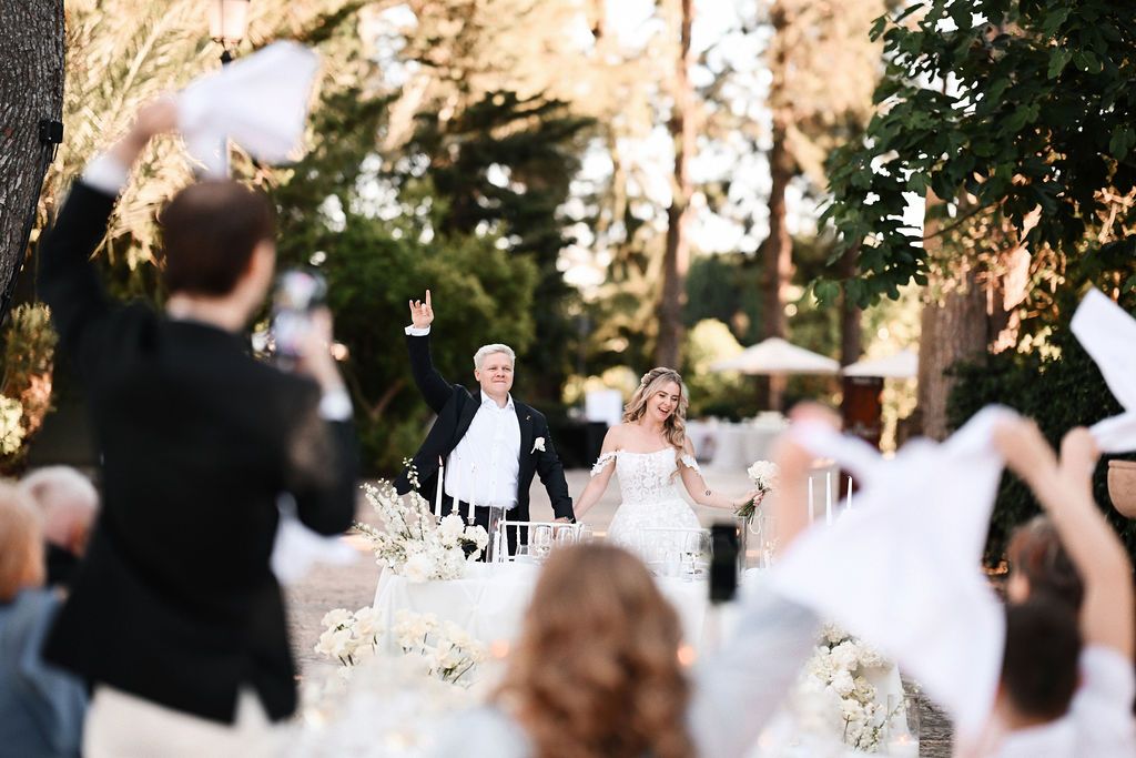 The bride and groom entering the wedding banquet as guests wave handkerchiefs at Finca El Senyoret. Festive Benidorm wedding memories.