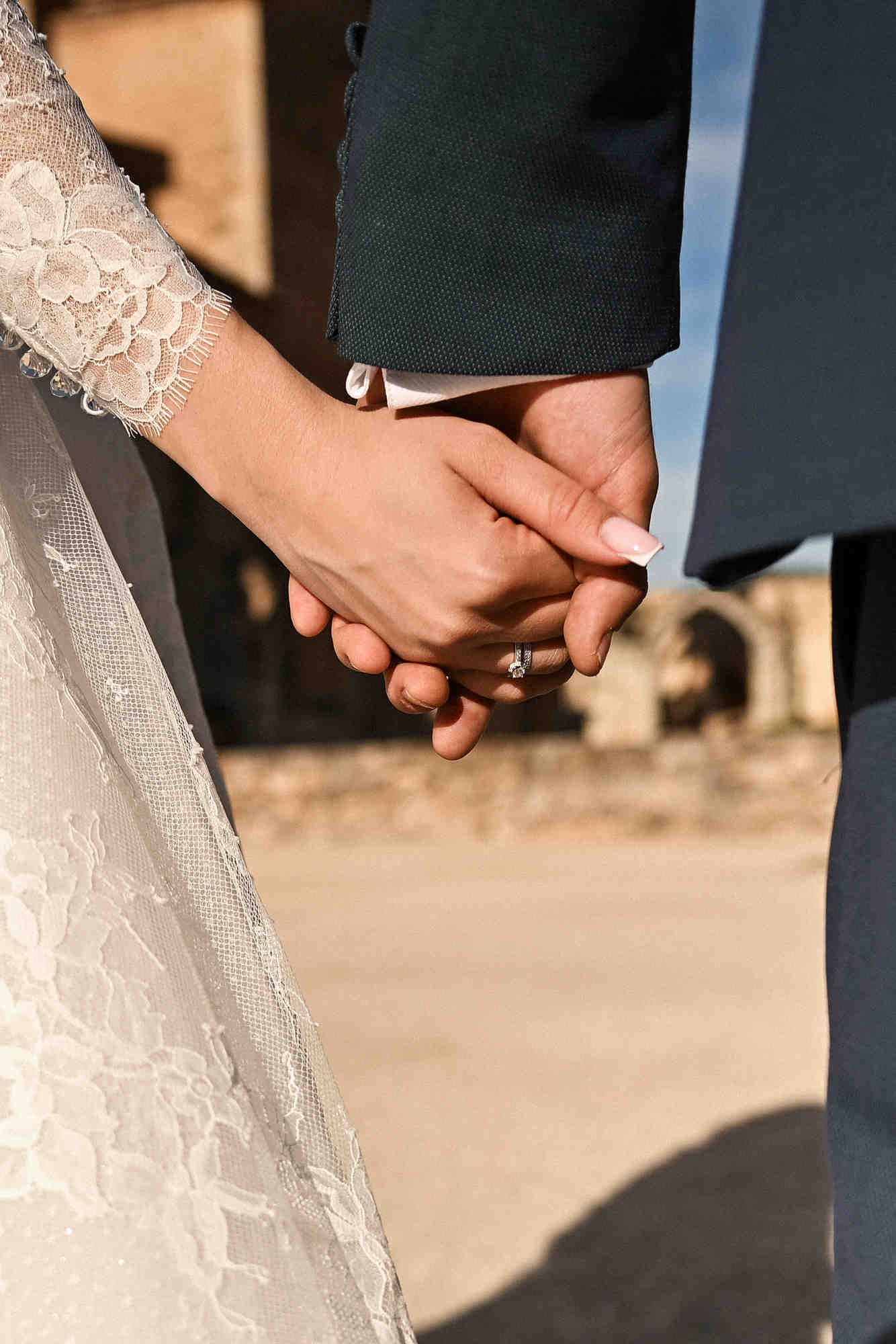 Detailed close-up of a wedding ring and the intertwined hands of the bride and groom during their ceremony at a historic Spanish monastery.