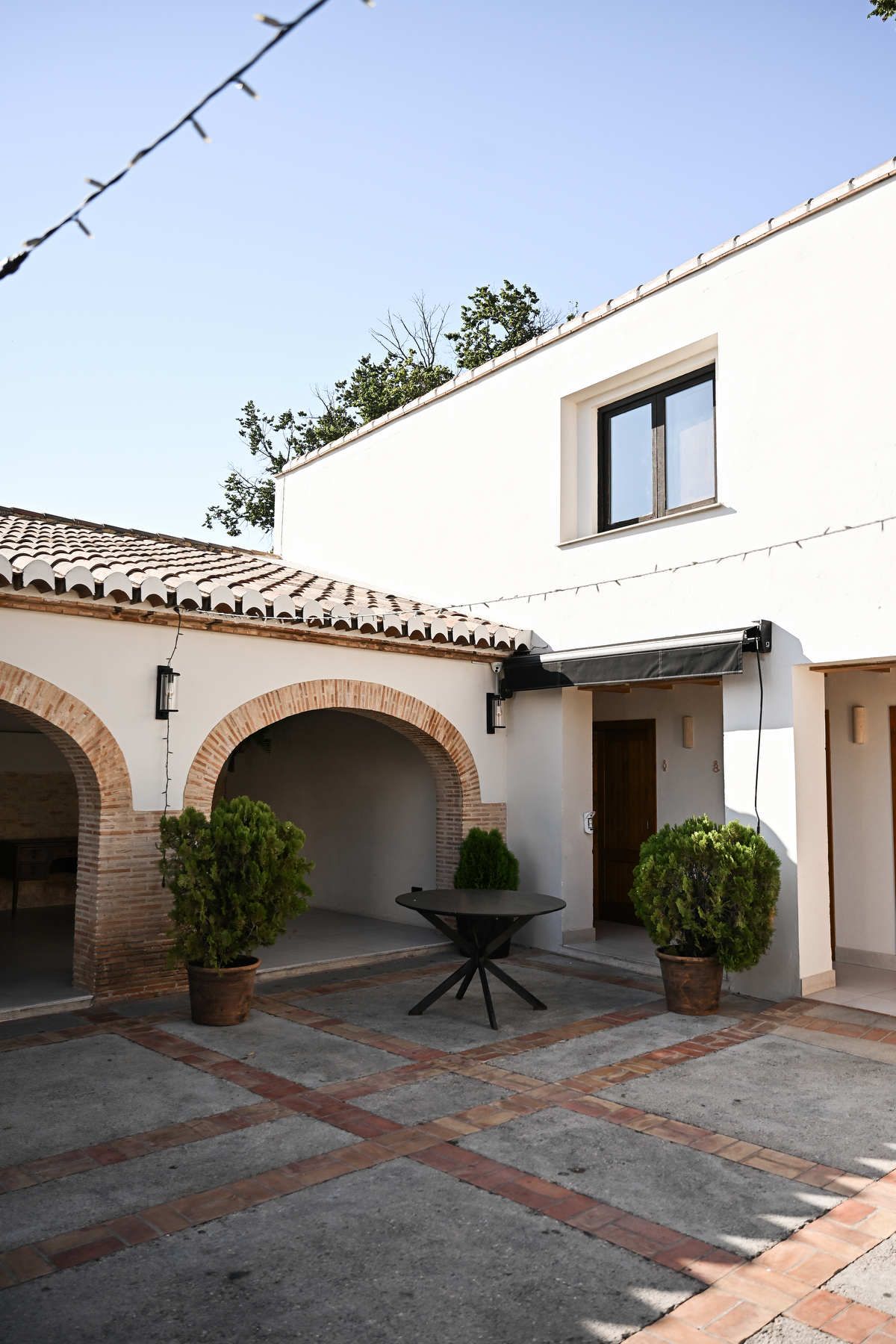 Mediterranean style courtyard Patio de Arcos at Alquería Kukala with brick arches and potted plants.