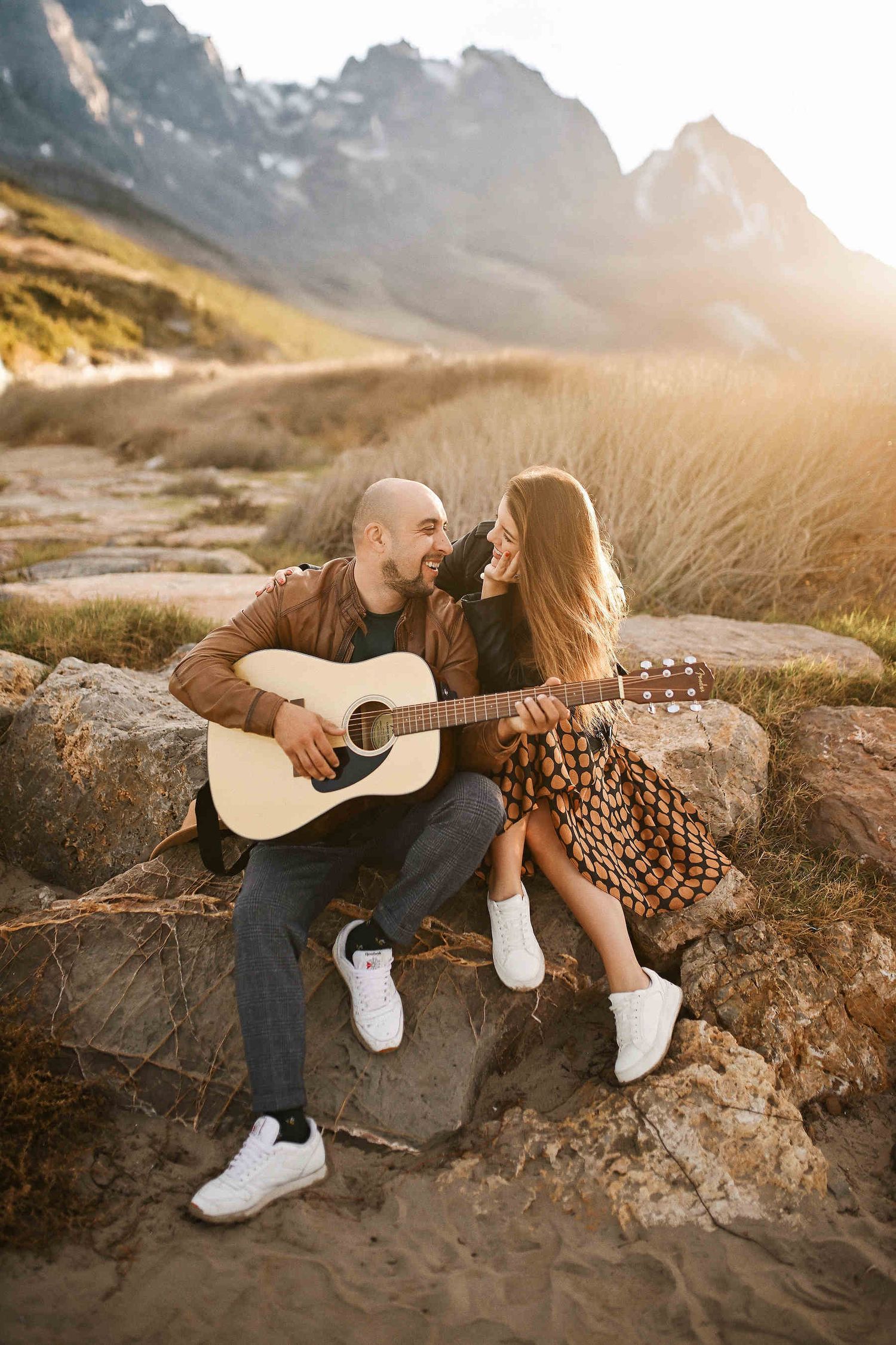 Couple hugging and playing guitar with beach and mountains in the background during a pre-wedding photoshoot in Valencia El Saler beach