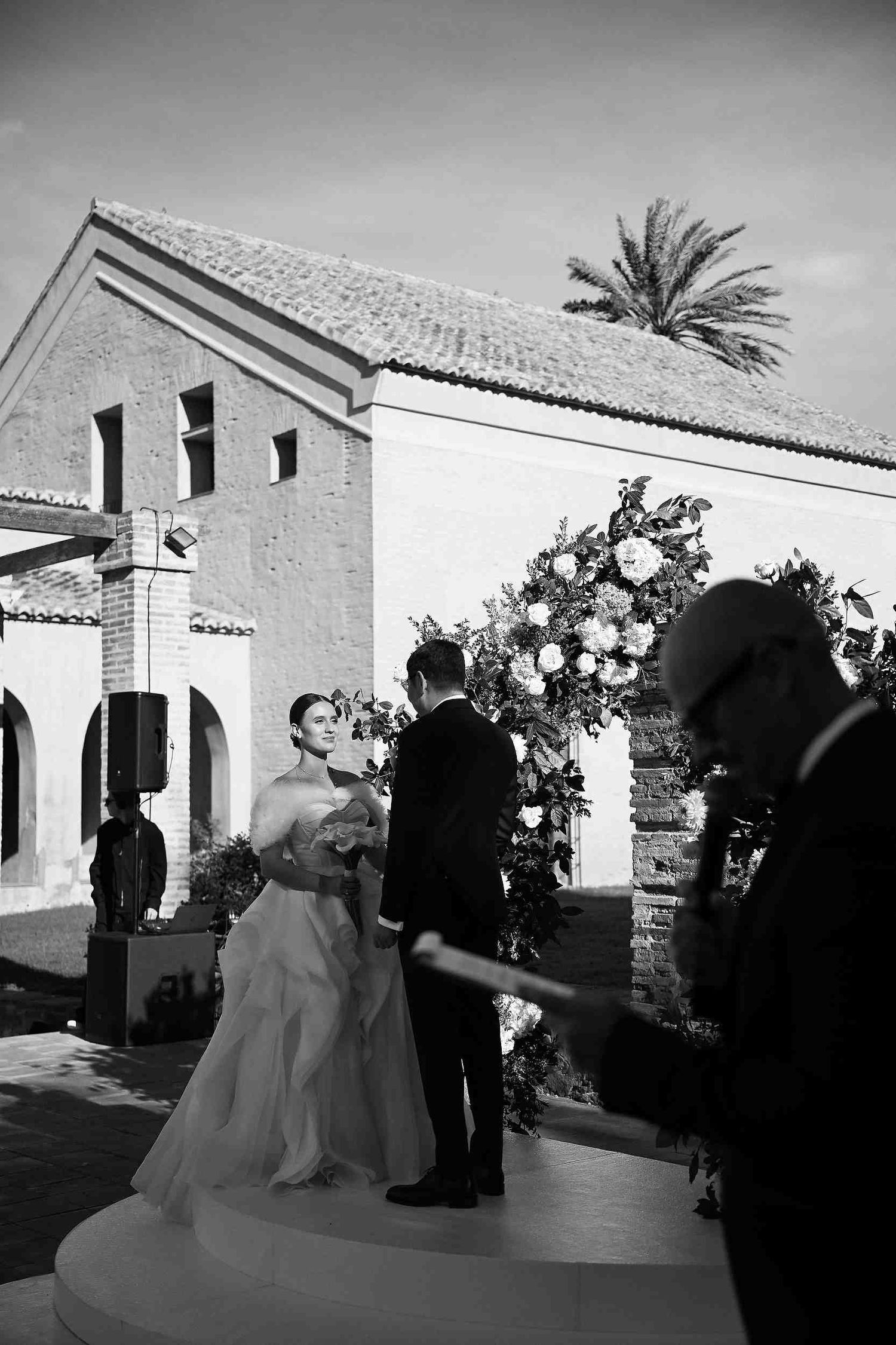 Bride and groom standing at the altar in the grand courtyard of La Cartoixa d'Ara Christi during their luxury wedding ceremony.