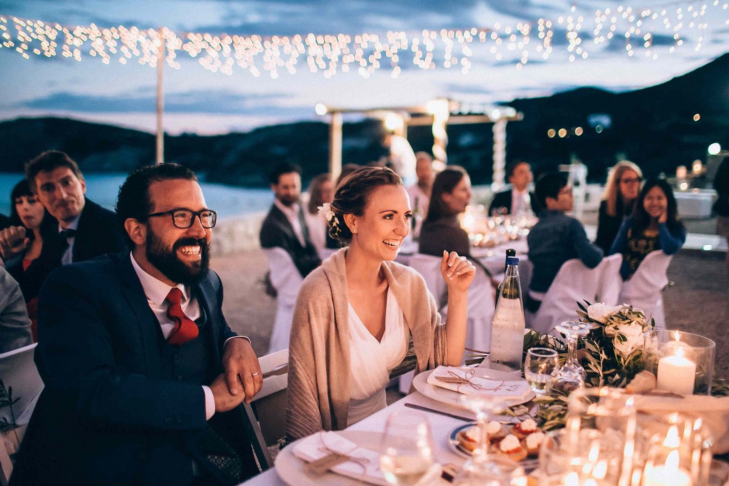 The newlyweds sitting at their decorated table surrounded by friends and family in Greece