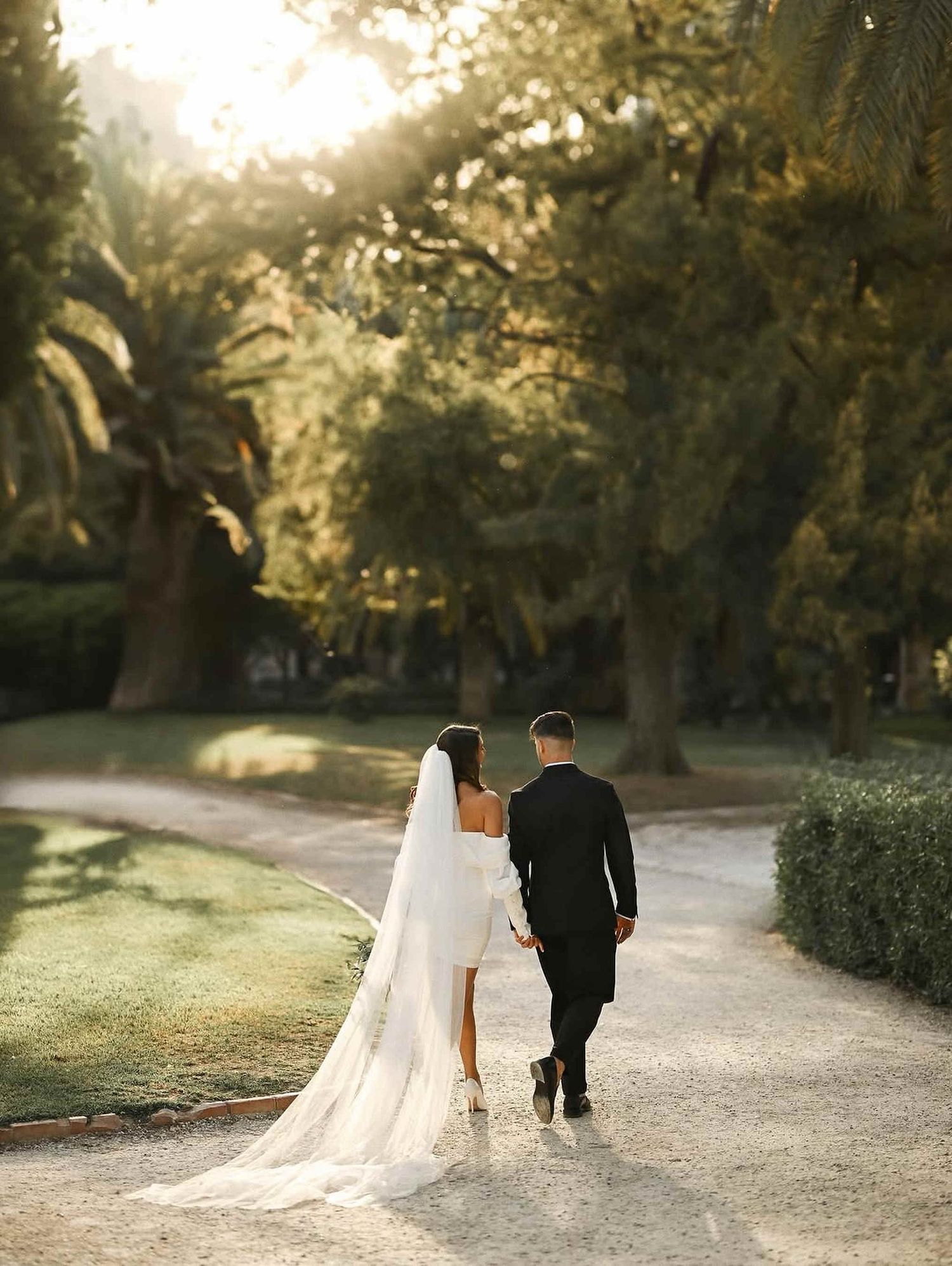 Sunset wedding photography in Spain. A romantic couple walking through a lush park filled with palms and golden Mediterranean light