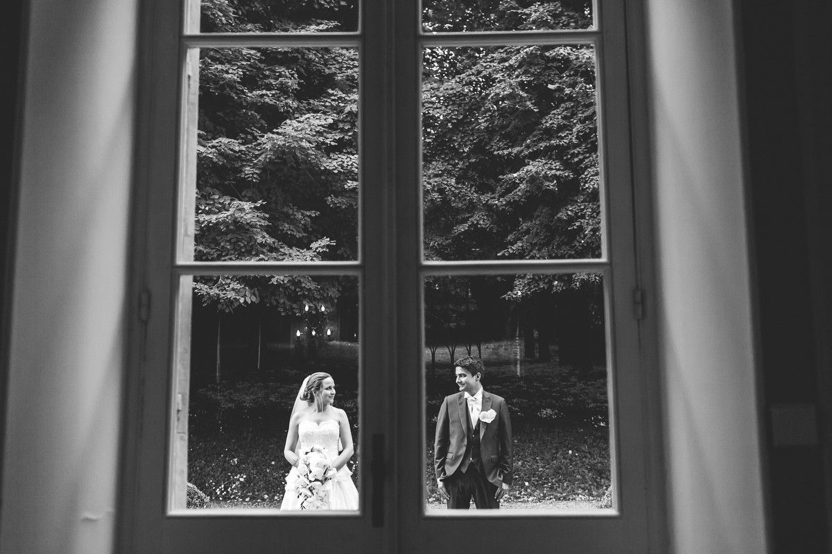 Black and white view of a bride and groom in the gardens, photographed through the closed windows of Chateau de Changy.