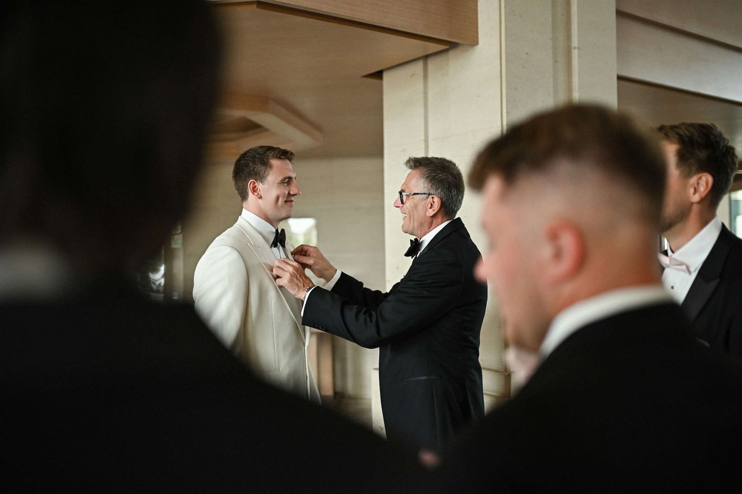 Father of the groom helping adjust a bowtie in the marble lobby of Hotel Las Arenas Balneario Resort