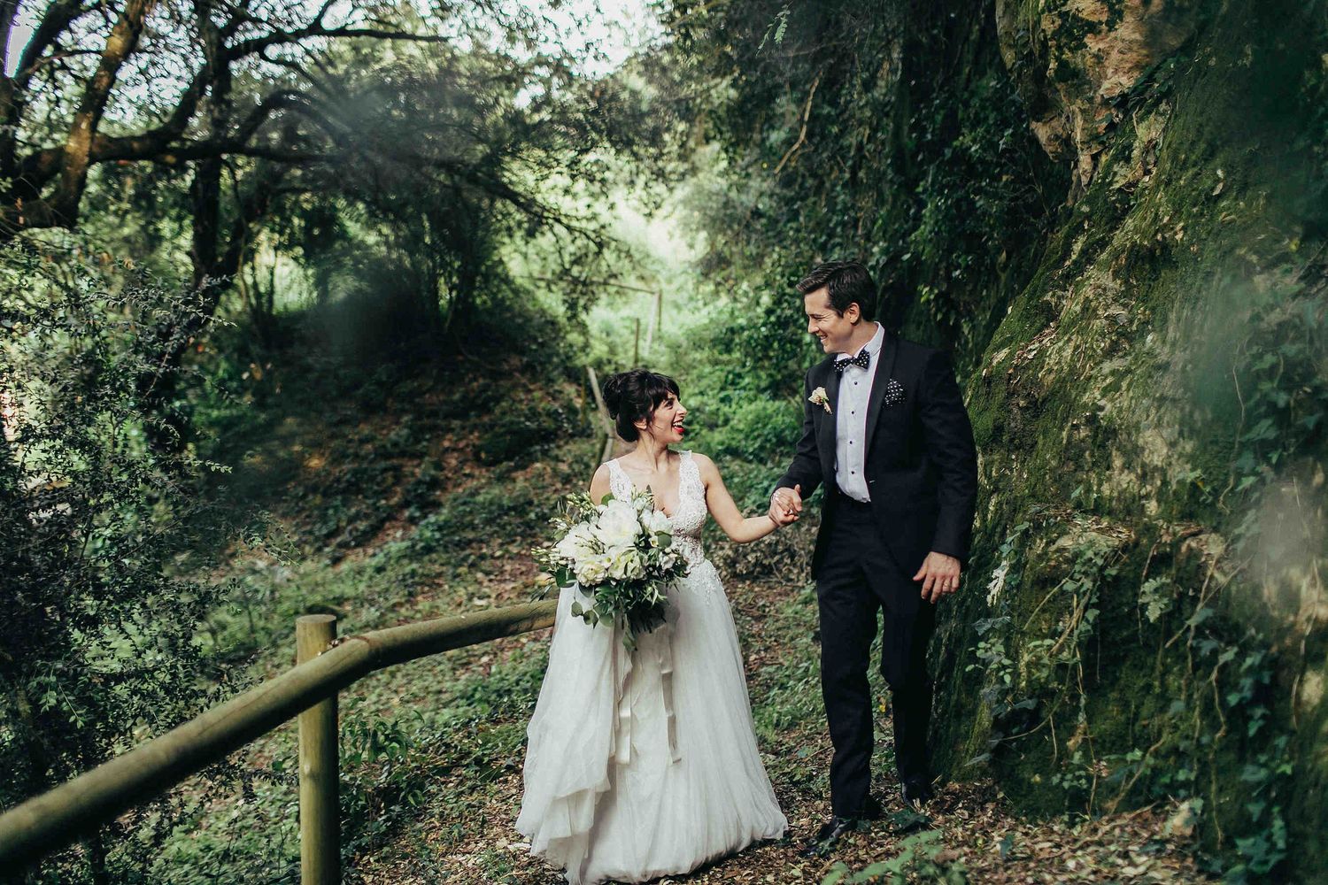 Wedding photographer in Barcelona. A couple walking against dramatic limestone cliffs and lush ivy at a historic Spanish villa estate