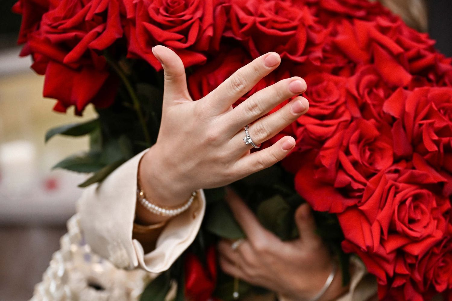 Close-up of a sparkling diamond engagement ring resting against a beautiful bouquet of red roses in Spain.