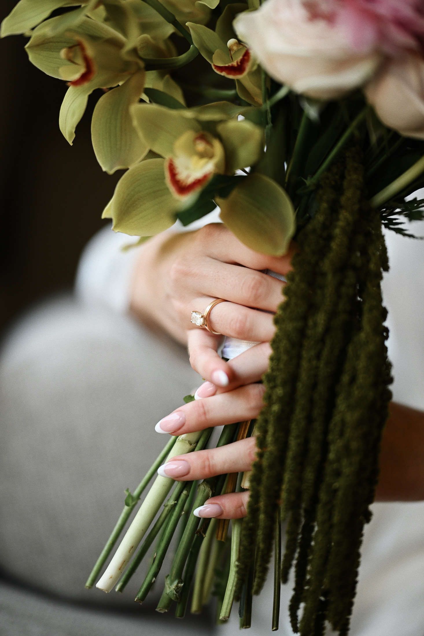Close-up of a luxury wedding ring on the bride's hand holding her elegant bridal bouquet during morning details photoshoot.