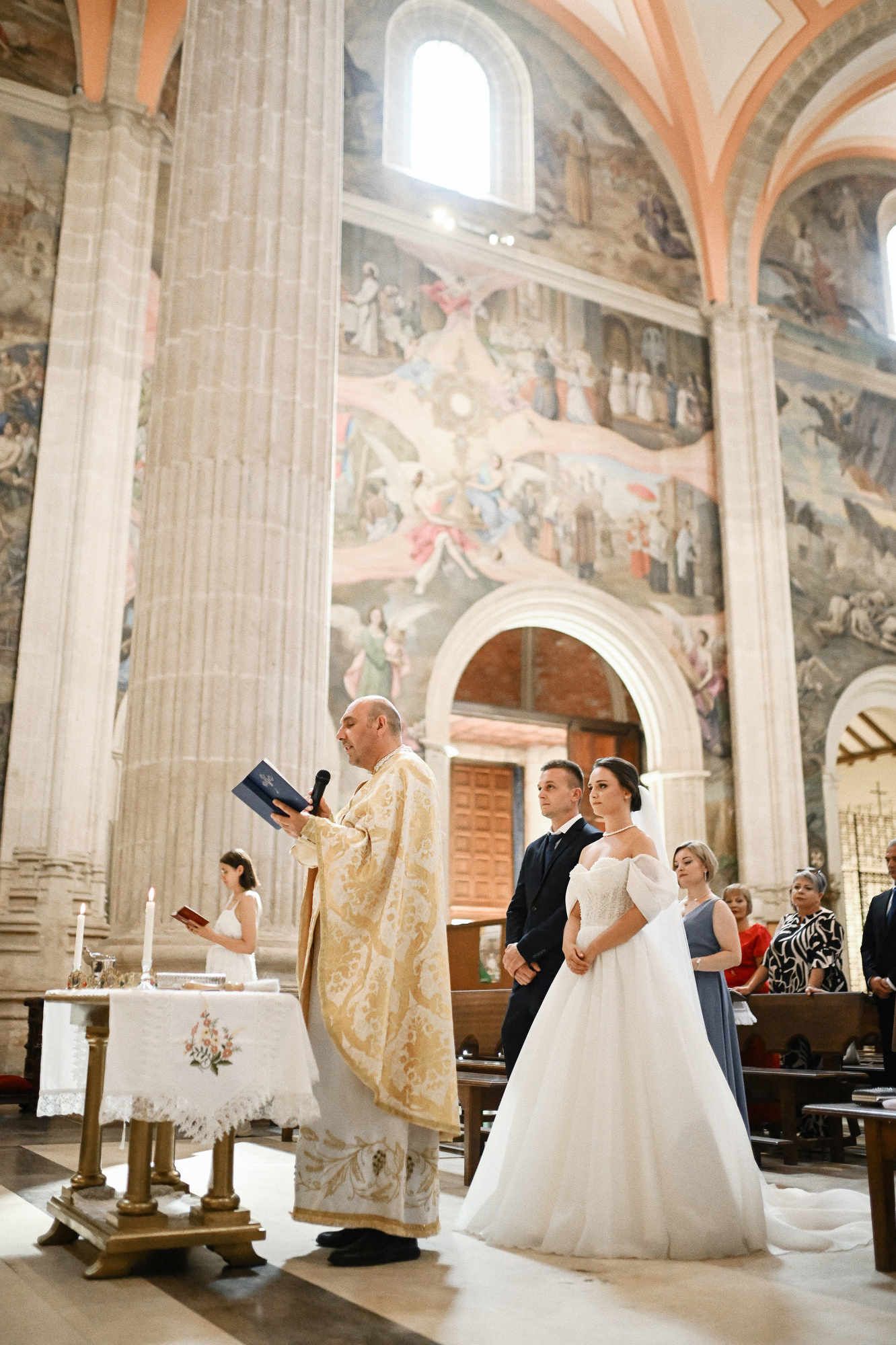 Bride and groom during their wedding ceremony, captured against the backdrop of historic, painted fresco walls inside the church.