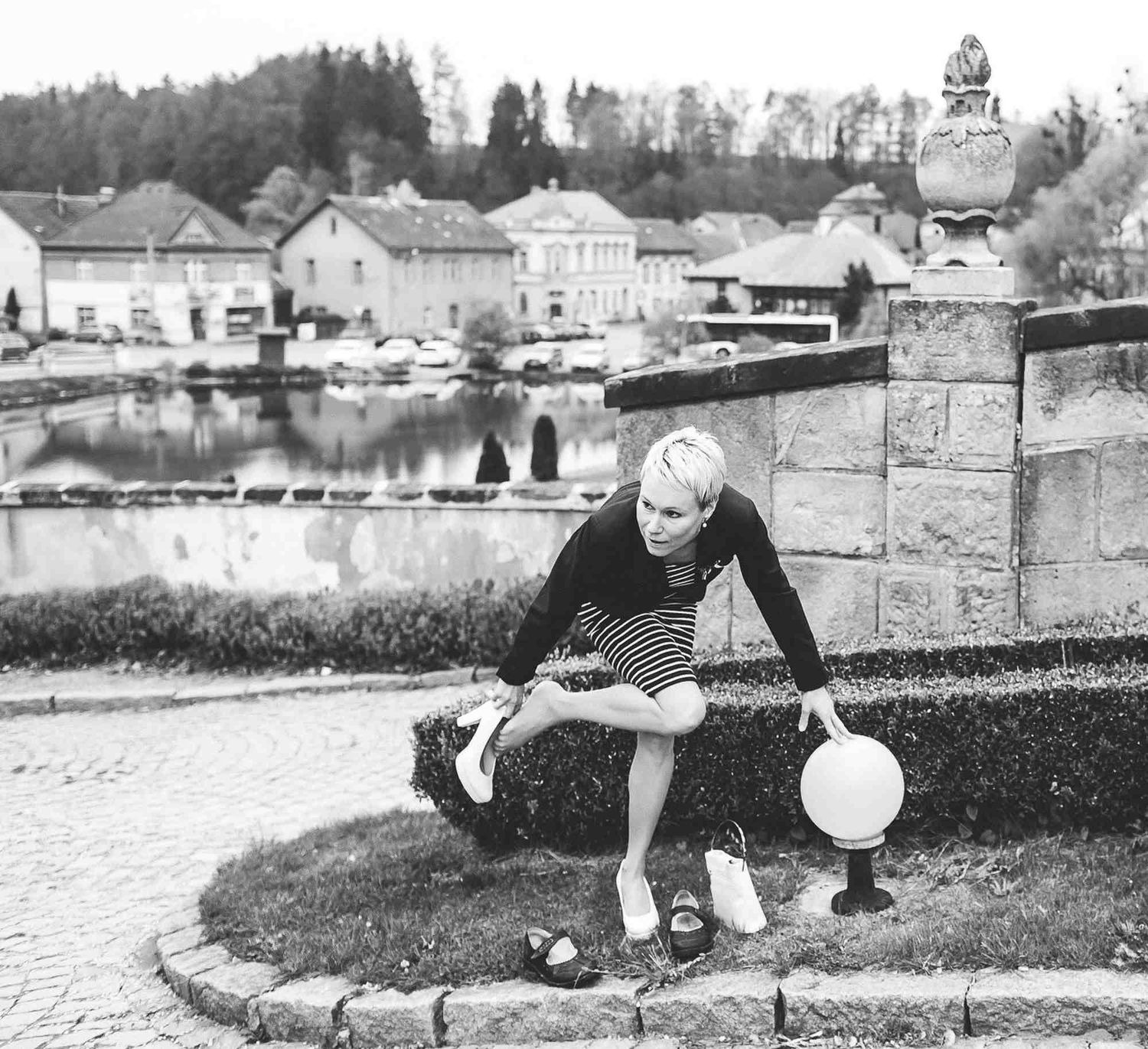 B&W documentary shot of a guest changing heels before the ceremony with a scenic Prague town view. Captured by a European photographer.