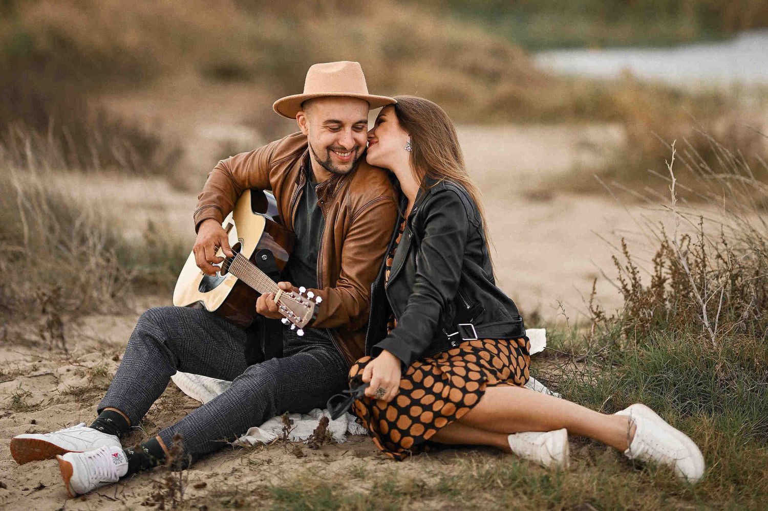 Engagement photographer Spain: A couple embracing on a beach blanket with a guitar and scenic mountain views during a coastal session.