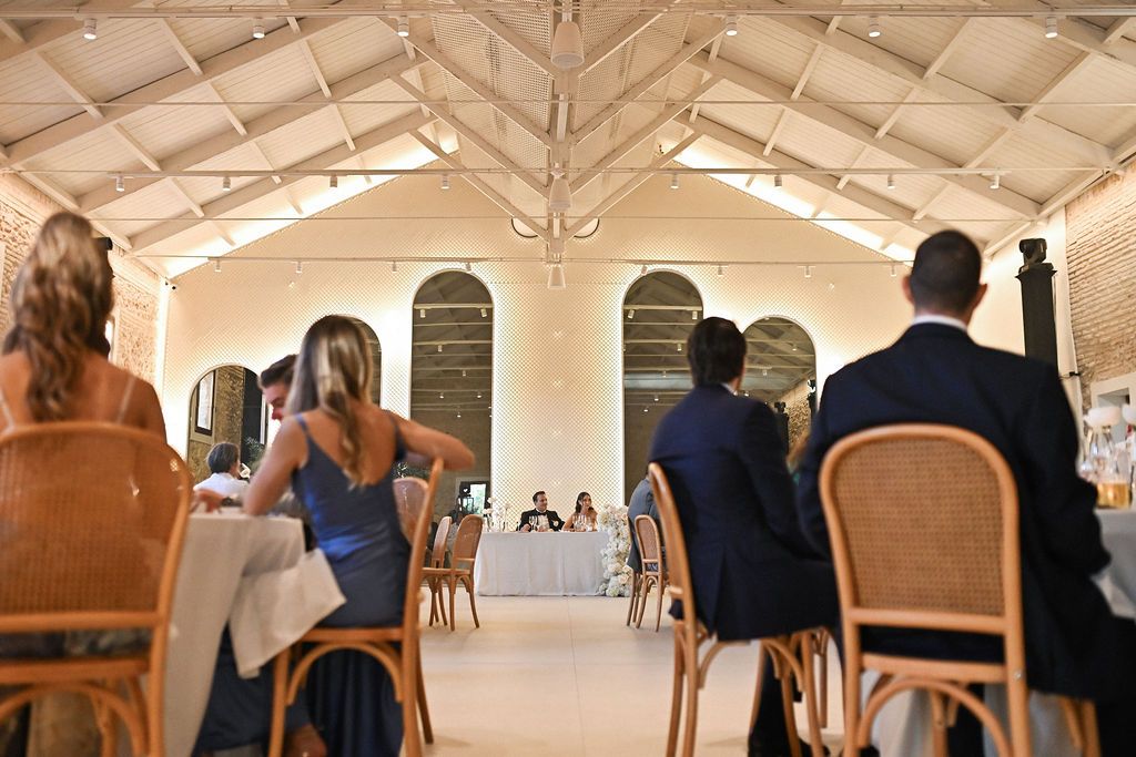 A view through the guests looking at the couple's raised central podium during a lively wedding celebration banquet at Finca del Canónigo.