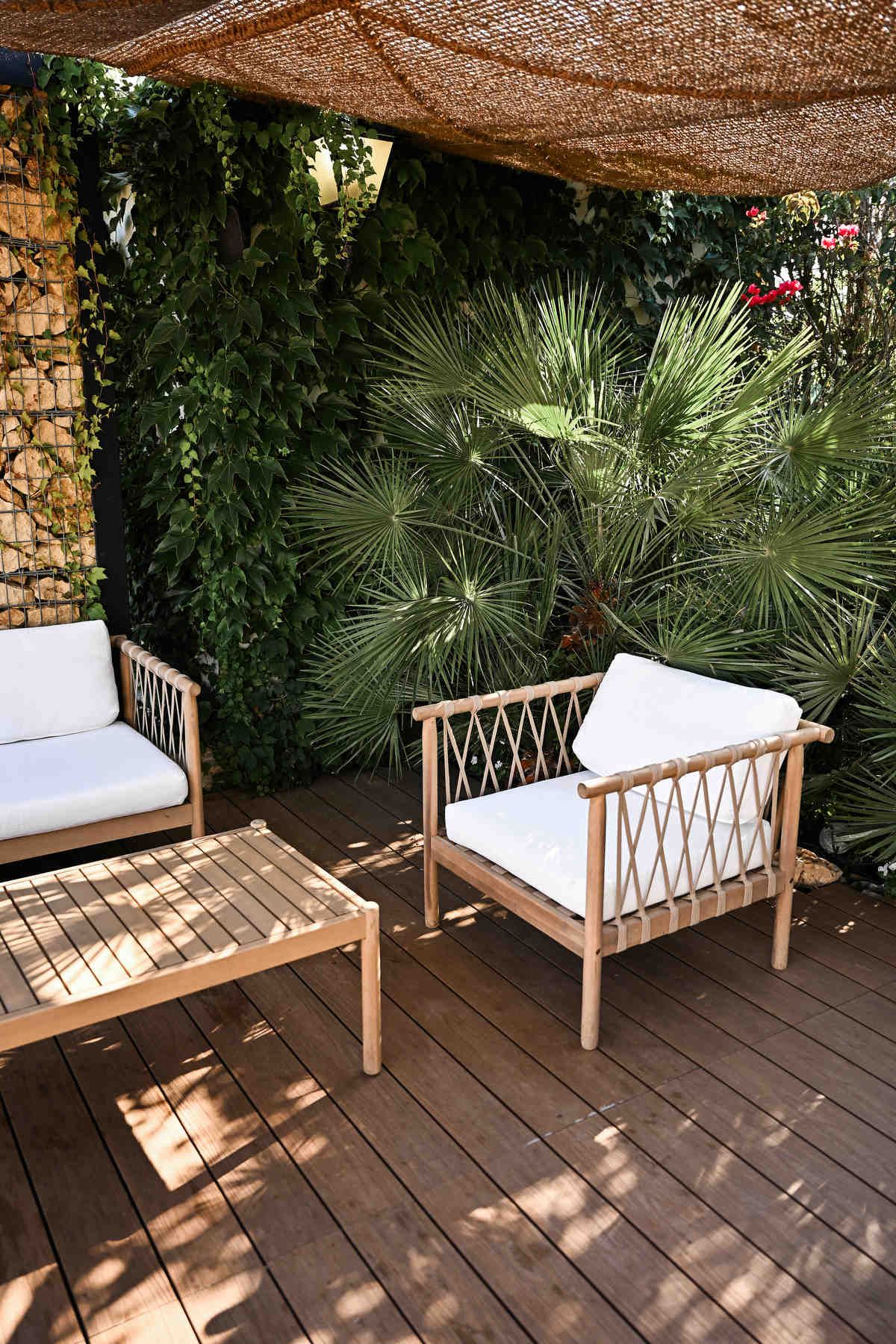 Wooden terrace lounge at Alquería Kukala with comfortable white armchairs, green palms, and a woven canopy.